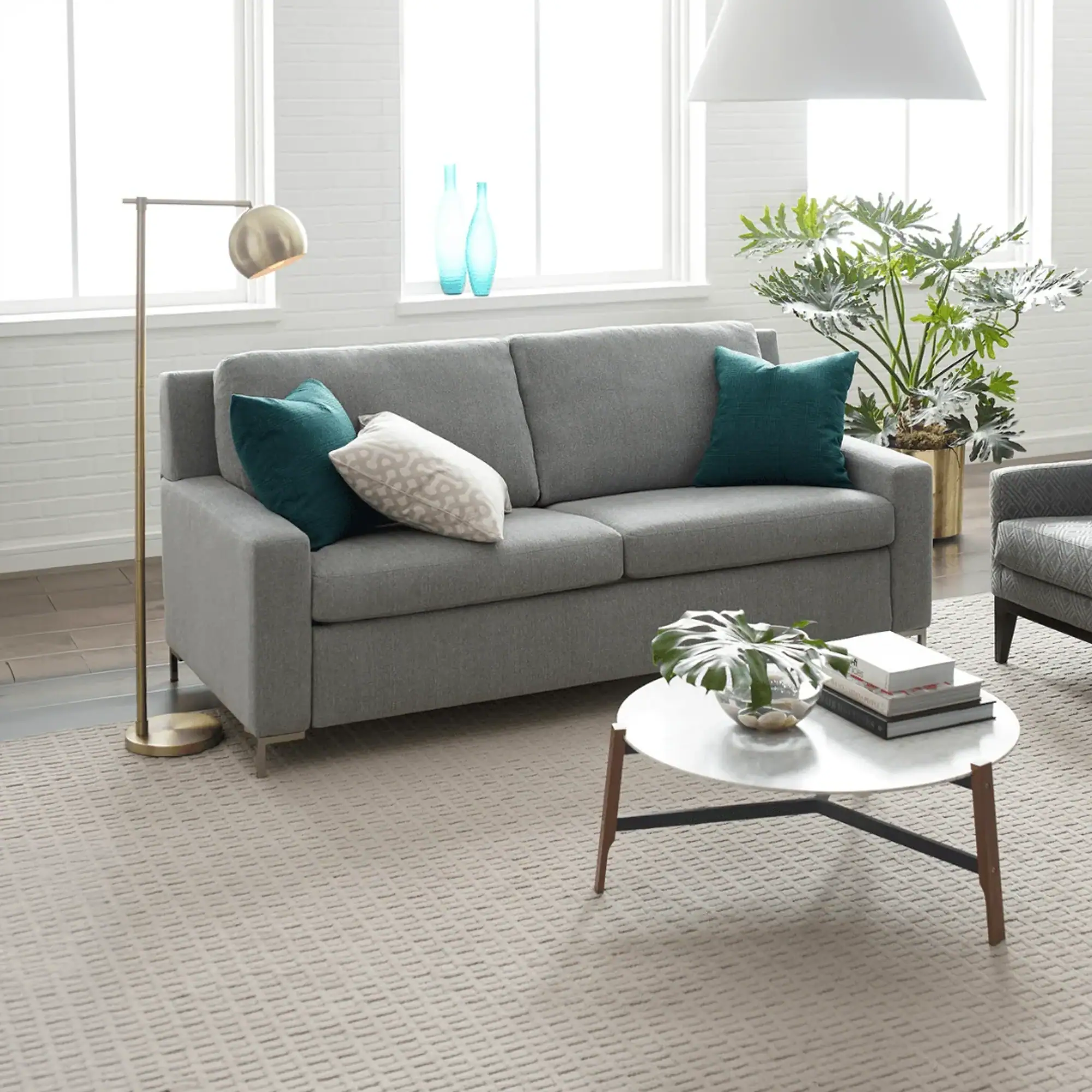 Bright living room with grey sofa, teal accent cushions, and natural sunlight from large windows.