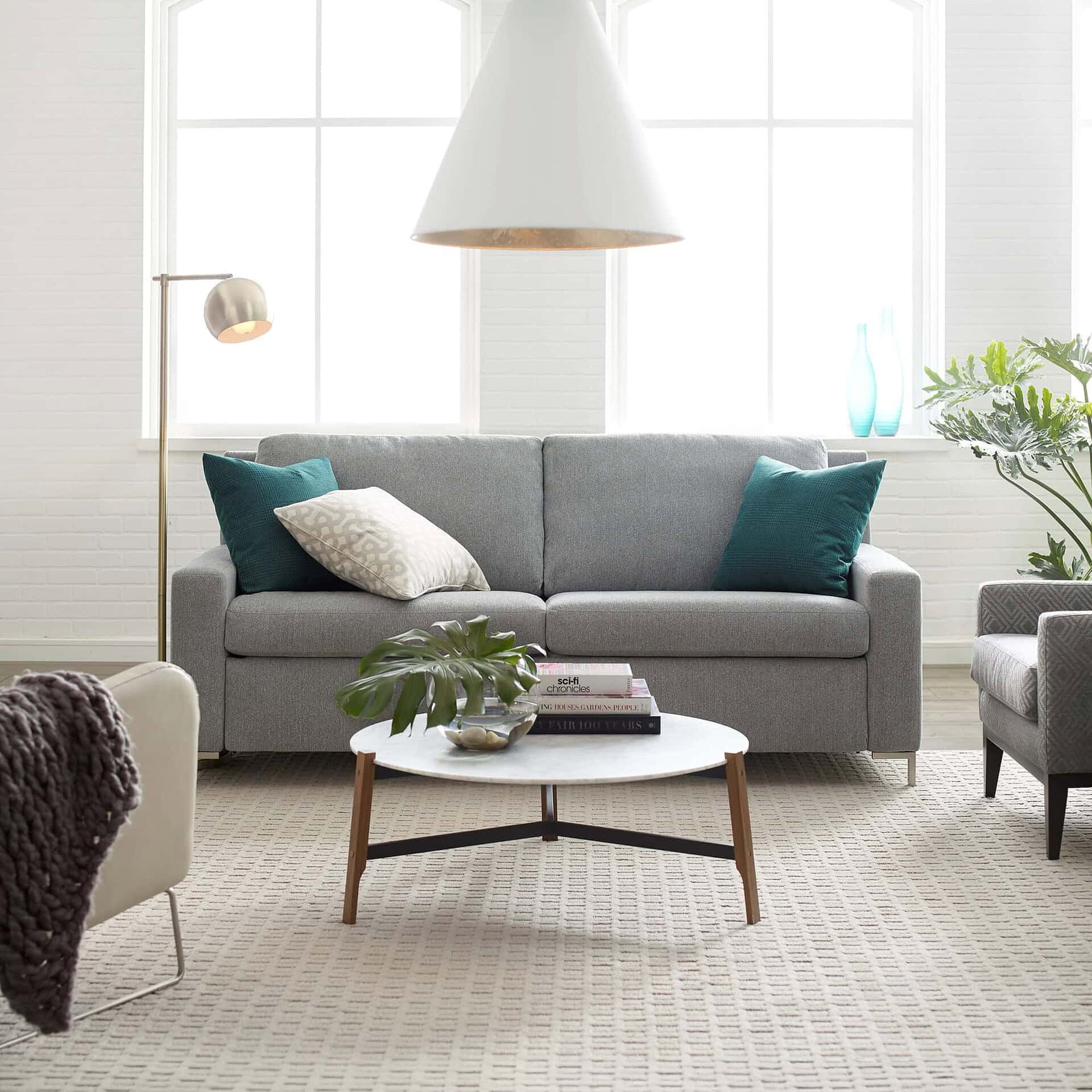 Bright living room with grey sofa, teal accent cushions, and natural sunlight from large windows.