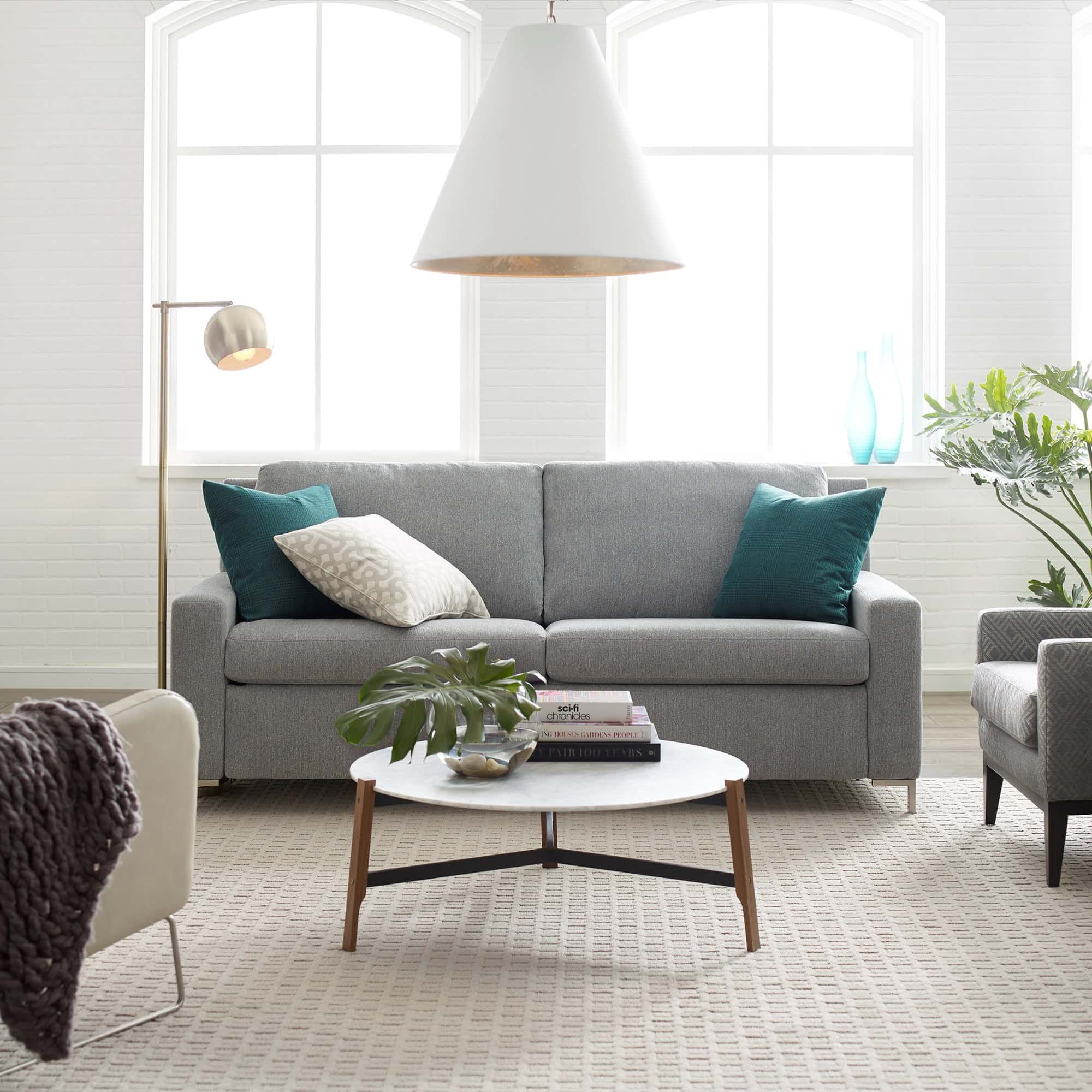 Bright living room with grey sofa, teal accent cushions, and natural sunlight from large windows.