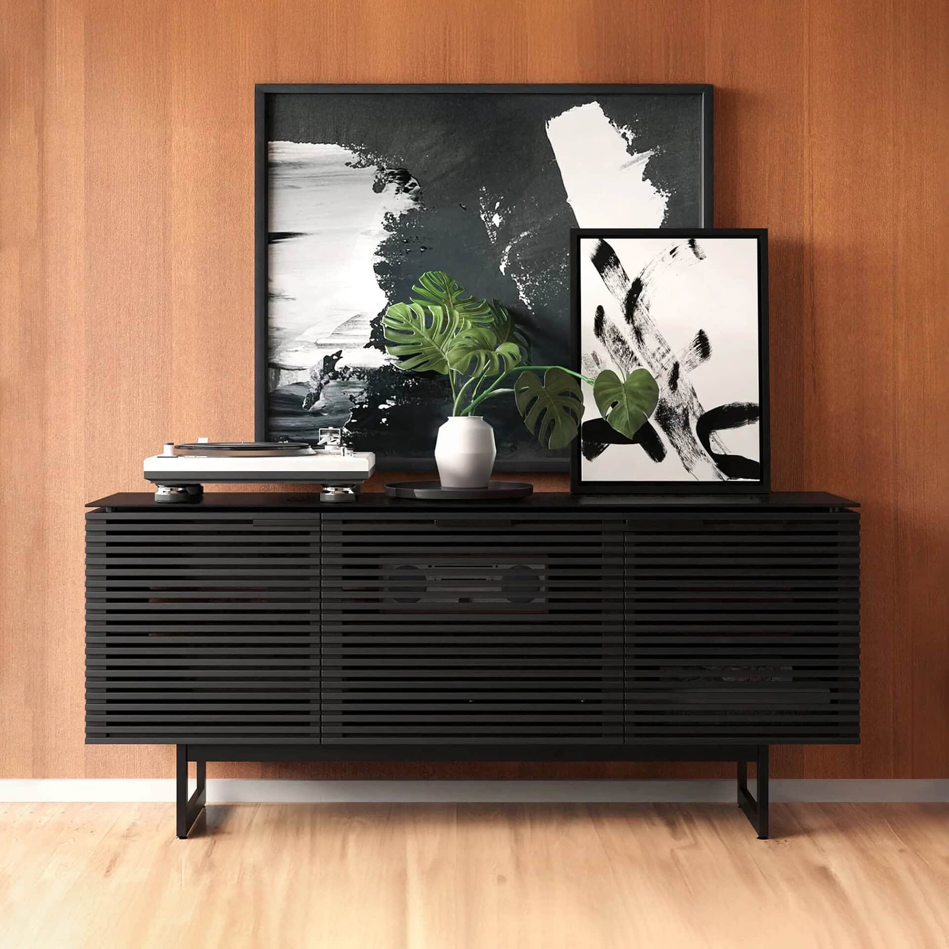 Sleek black modern sideboard with slatted design, decorative artwork, and plant in a stylish living room setting.