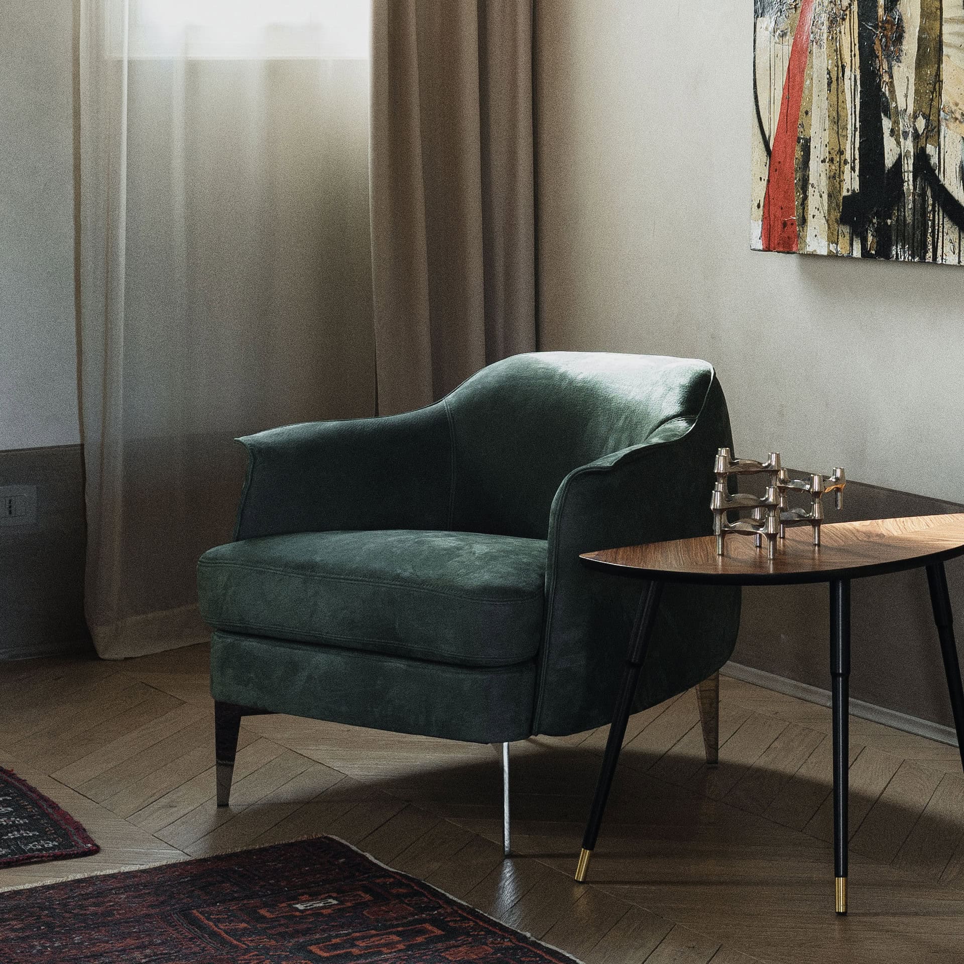 Green velvet Bohème Upholstered Lounge Armchair with slim black metal legs, placed beside a round wooden side table in a softly lit interior.