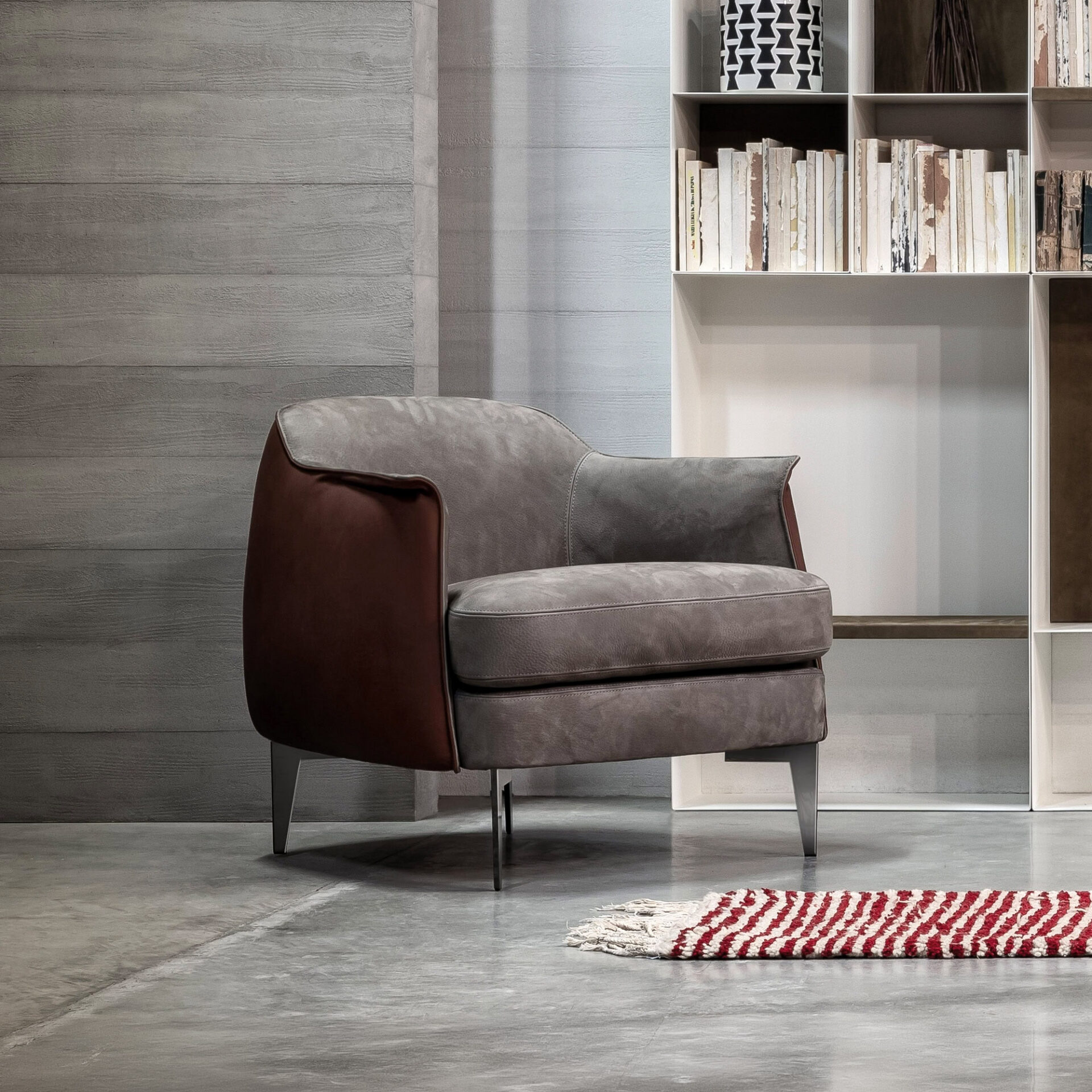 Bohème Upholstered Lounge Armchair with contrasting brown leather sides and gray fabric seat, styled in a minimalist room with shelving and modern décor.