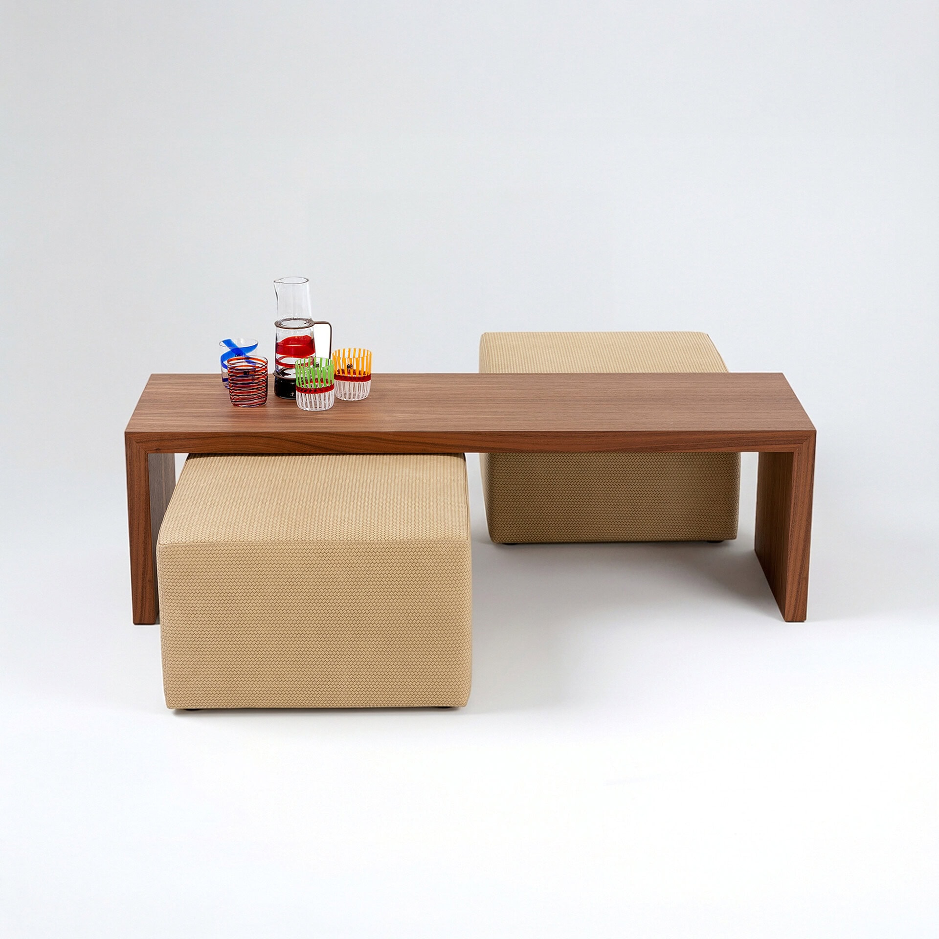 Elegant wooden dining table with beige upholstered stools and vibrant glassware.