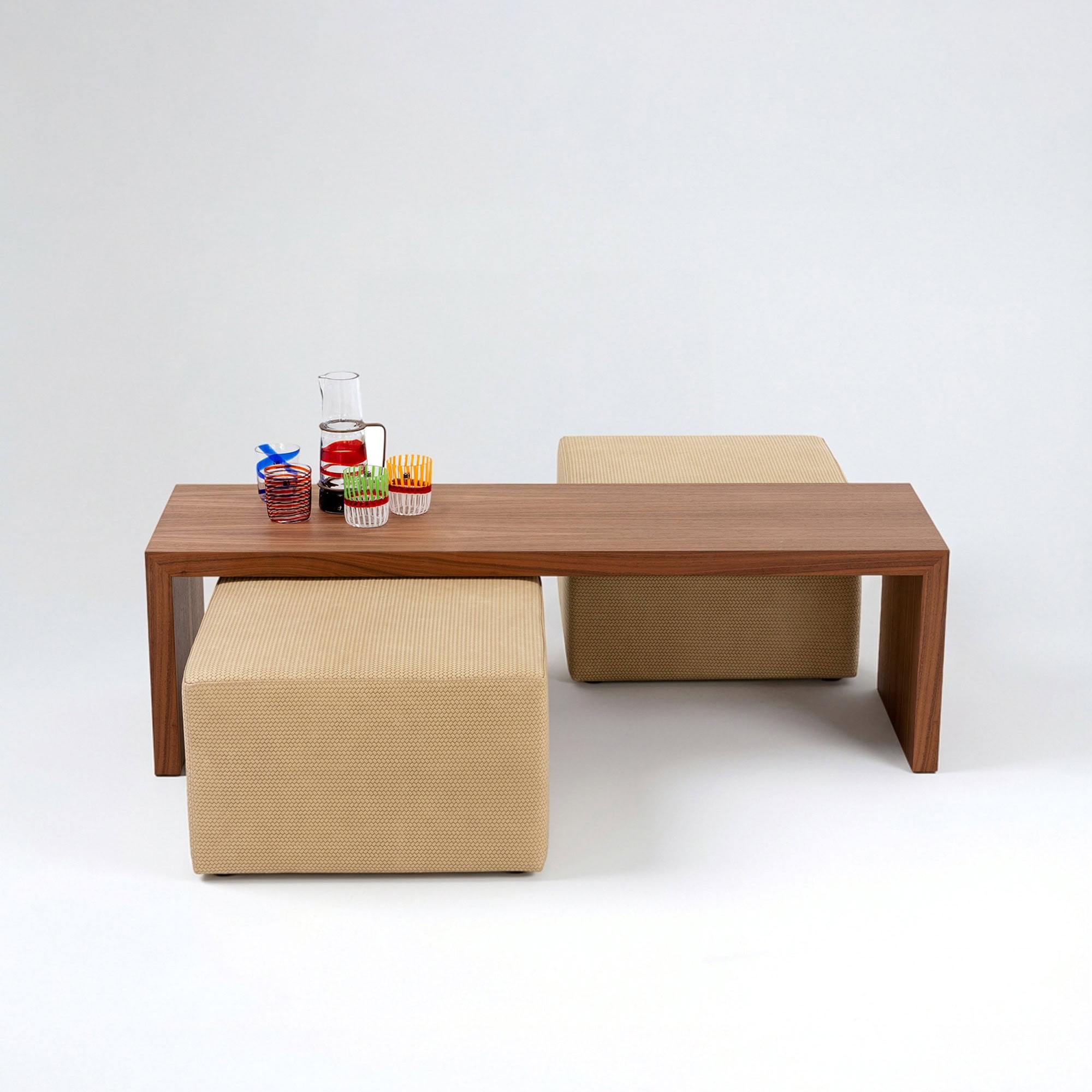 Elegant wooden dining table with beige upholstered stools and vibrant glassware.