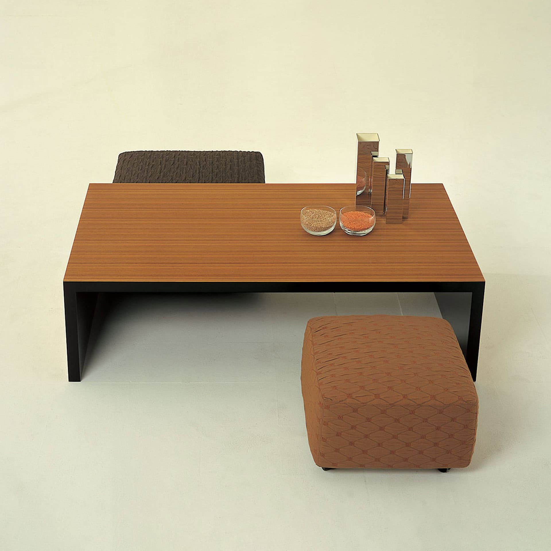 Modern wooden desk with ottoman and decorative objects in a minimalistic setting.