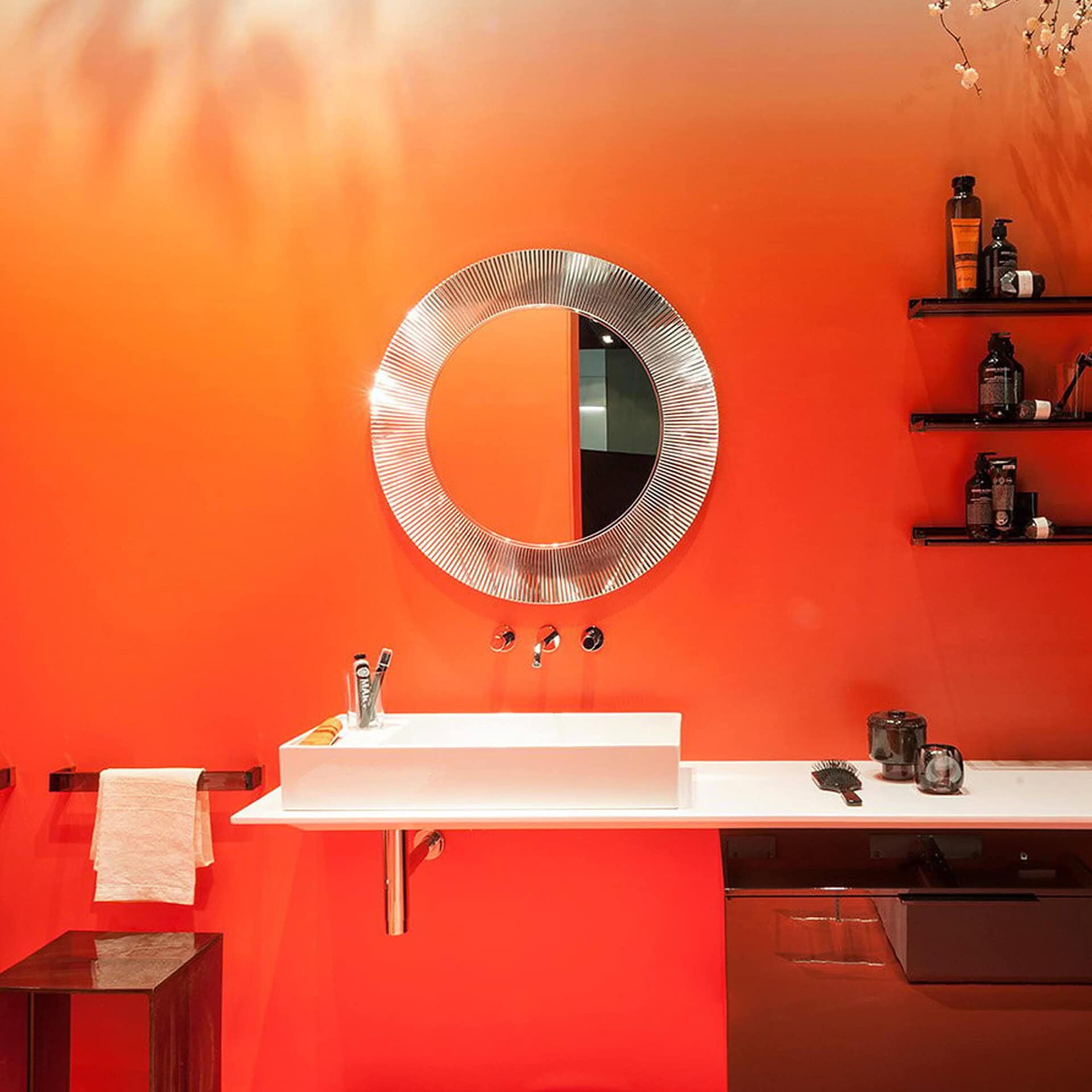 Kartell All Saints round mirror with pleated amber frame illuminated in a modern bathroom setting.