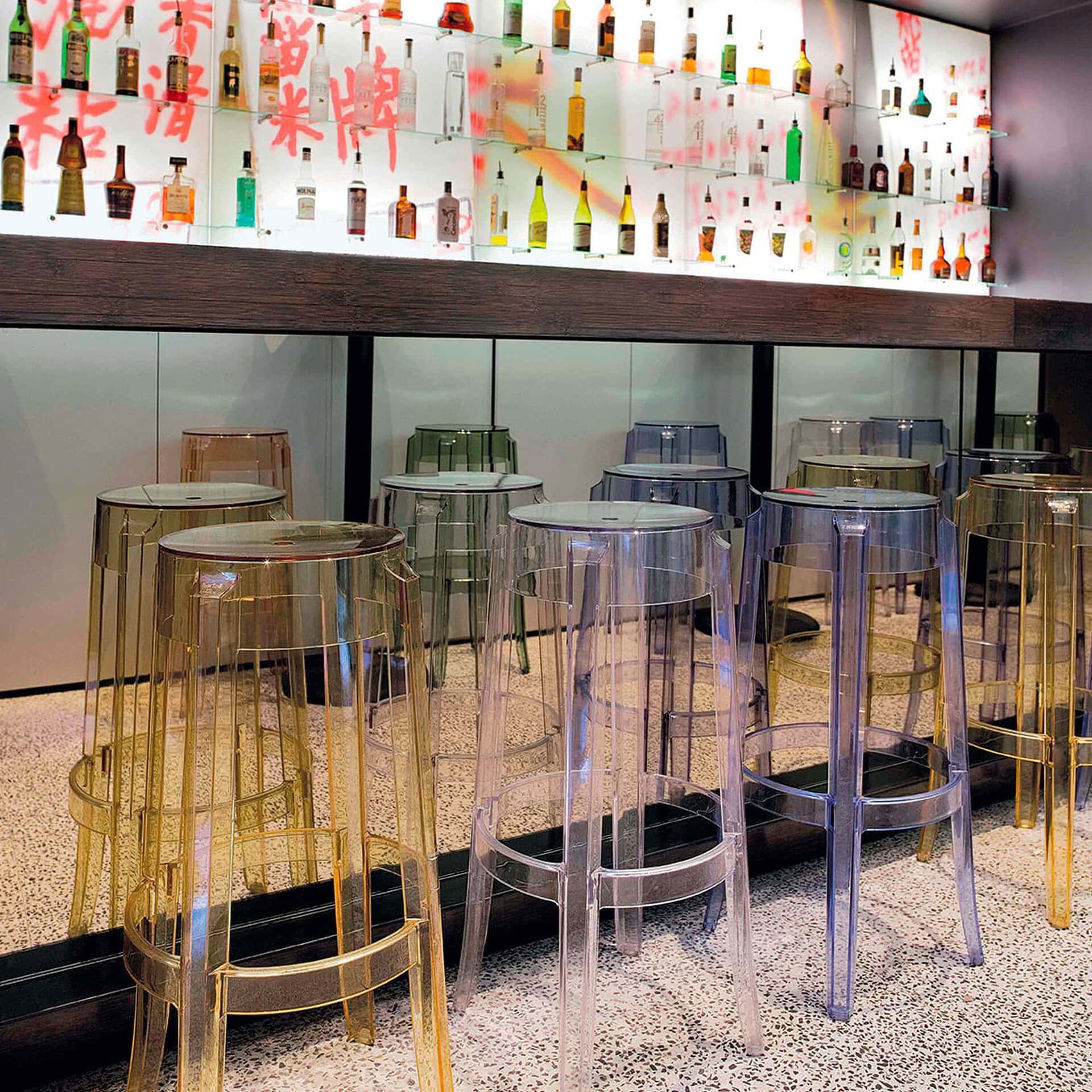 Amber Charles Ghost stools lined up along a bar in a contemporary restaurant.