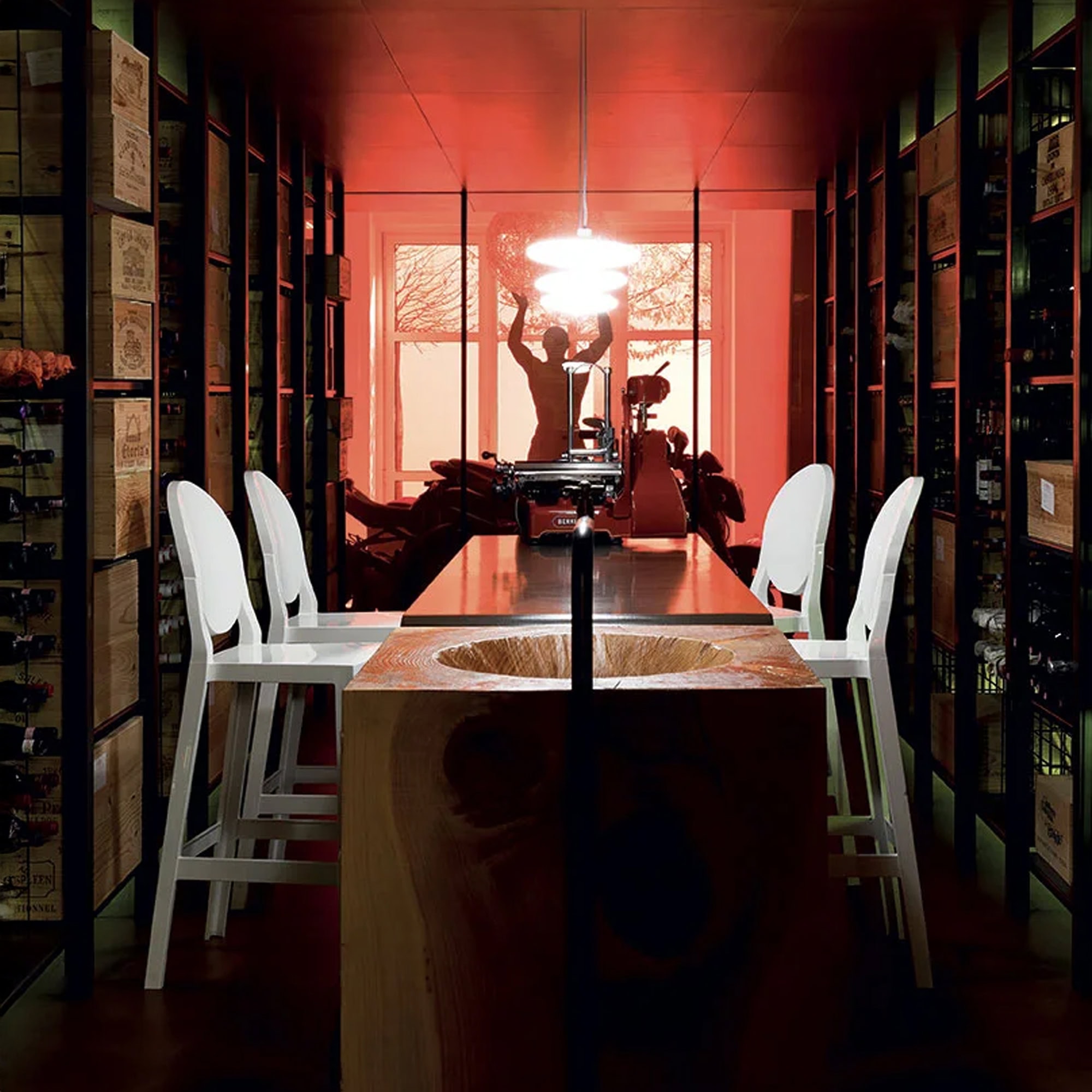 Dining room setting with Kartell One More stools around a dark wood table, accented by dramatic red wall lighting.