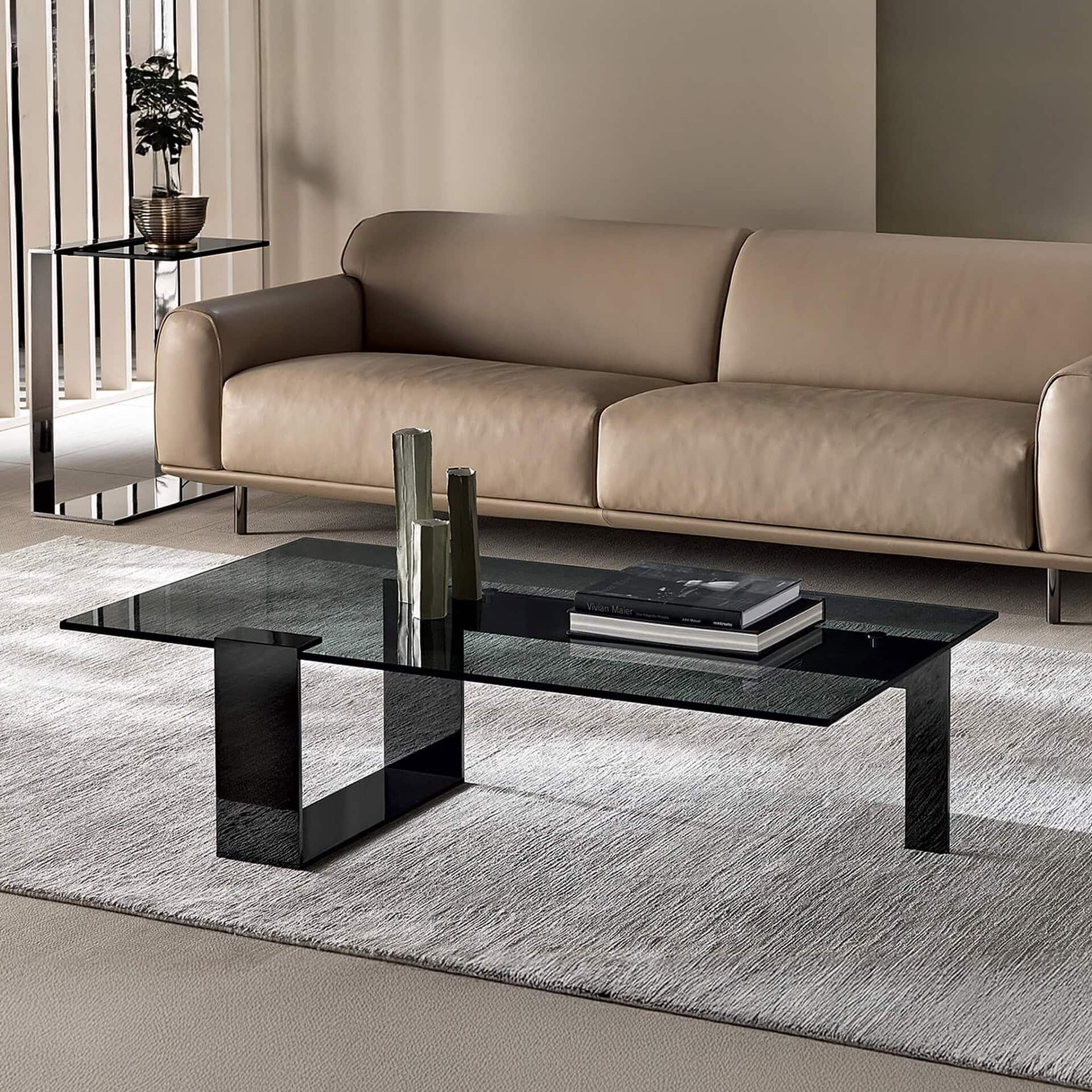 Plinsky Glass Low Coffee Table with black base and rectangular glass top styled in a modern living room with a beige sofa.