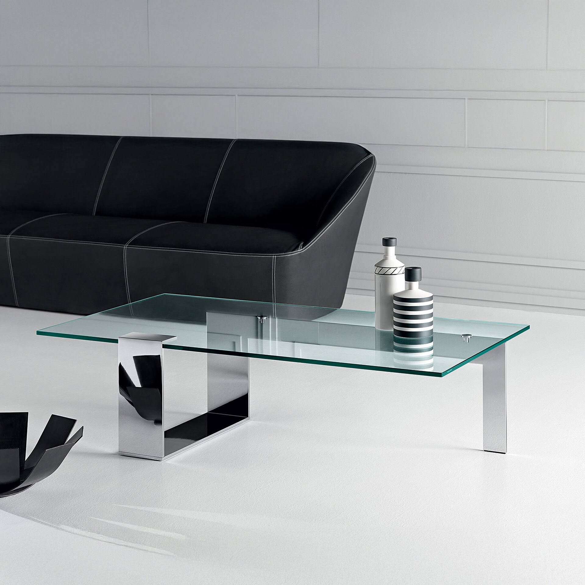Plinsky Glass Low Coffee Table with glass top and black lacquered metal base placed in a contemporary living room with a dark sofa.