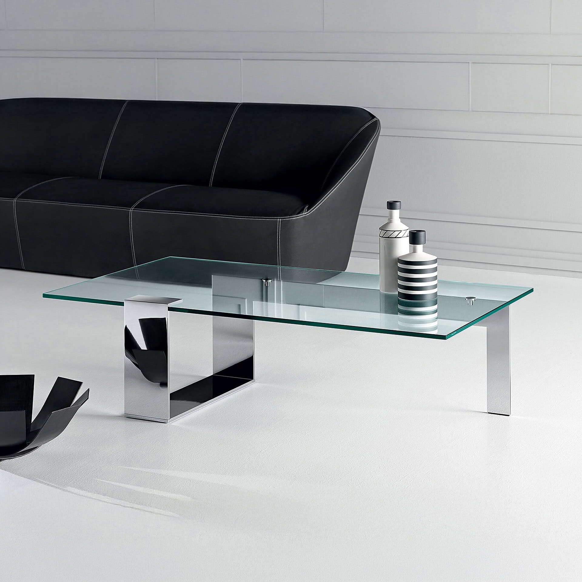 Plinsky Glass Low Coffee Table with glass top and black lacquered metal base placed in a contemporary living room with a dark sofa.