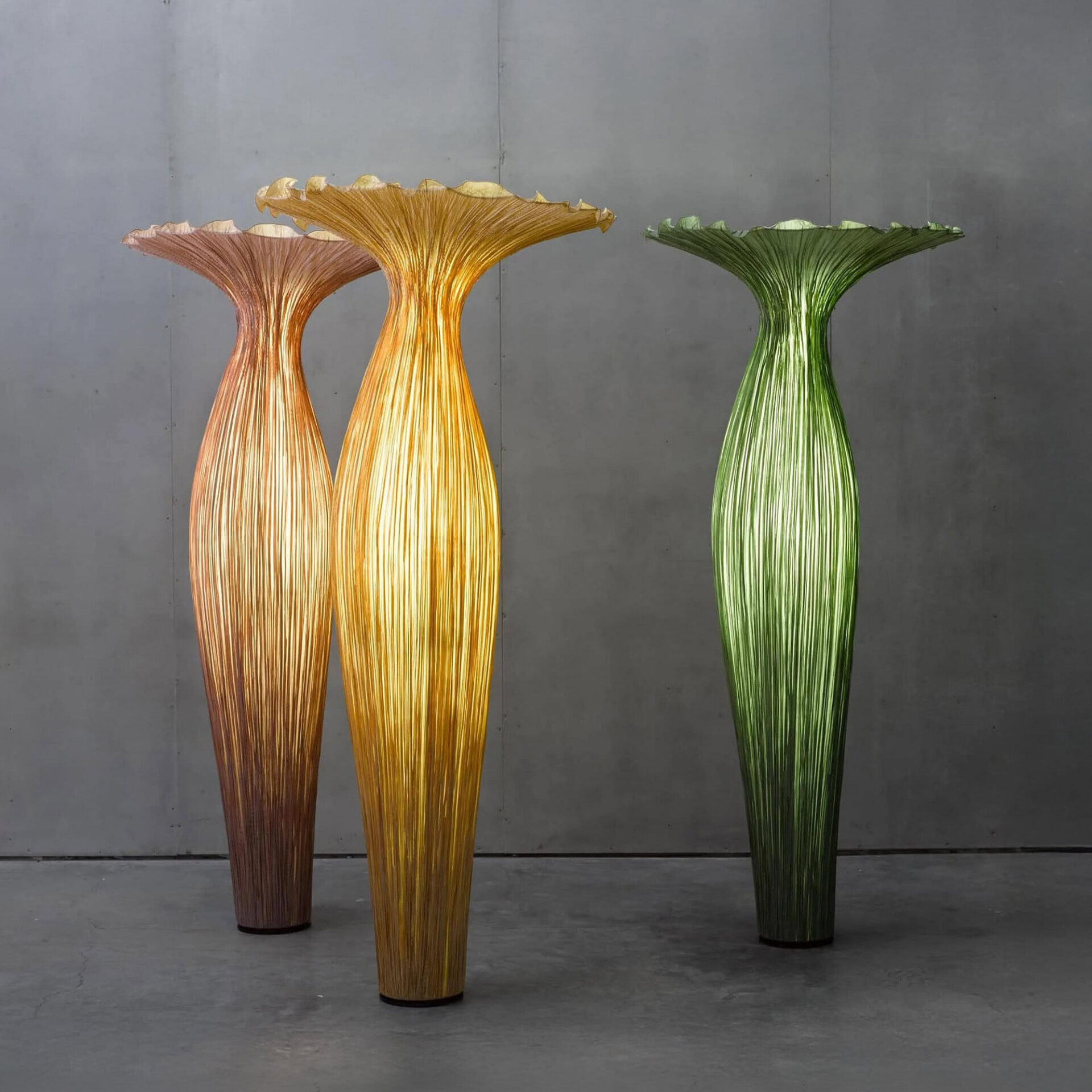 Two tall silk floor lamps in cream and green with sculptural flower-inspired shapes beside a sofa in a modern living room.