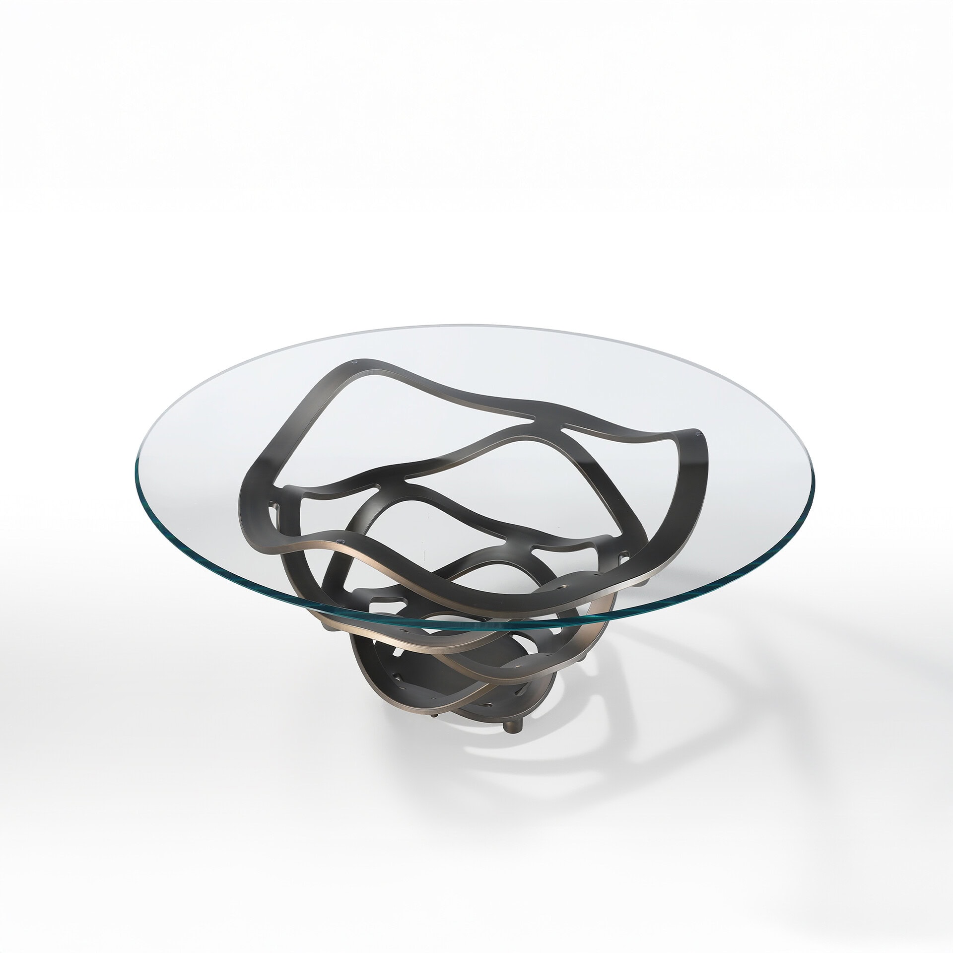 A round glass coffee table with a sculptural, dark metallic base featuring intertwining, wavy shapes, set against a white background.