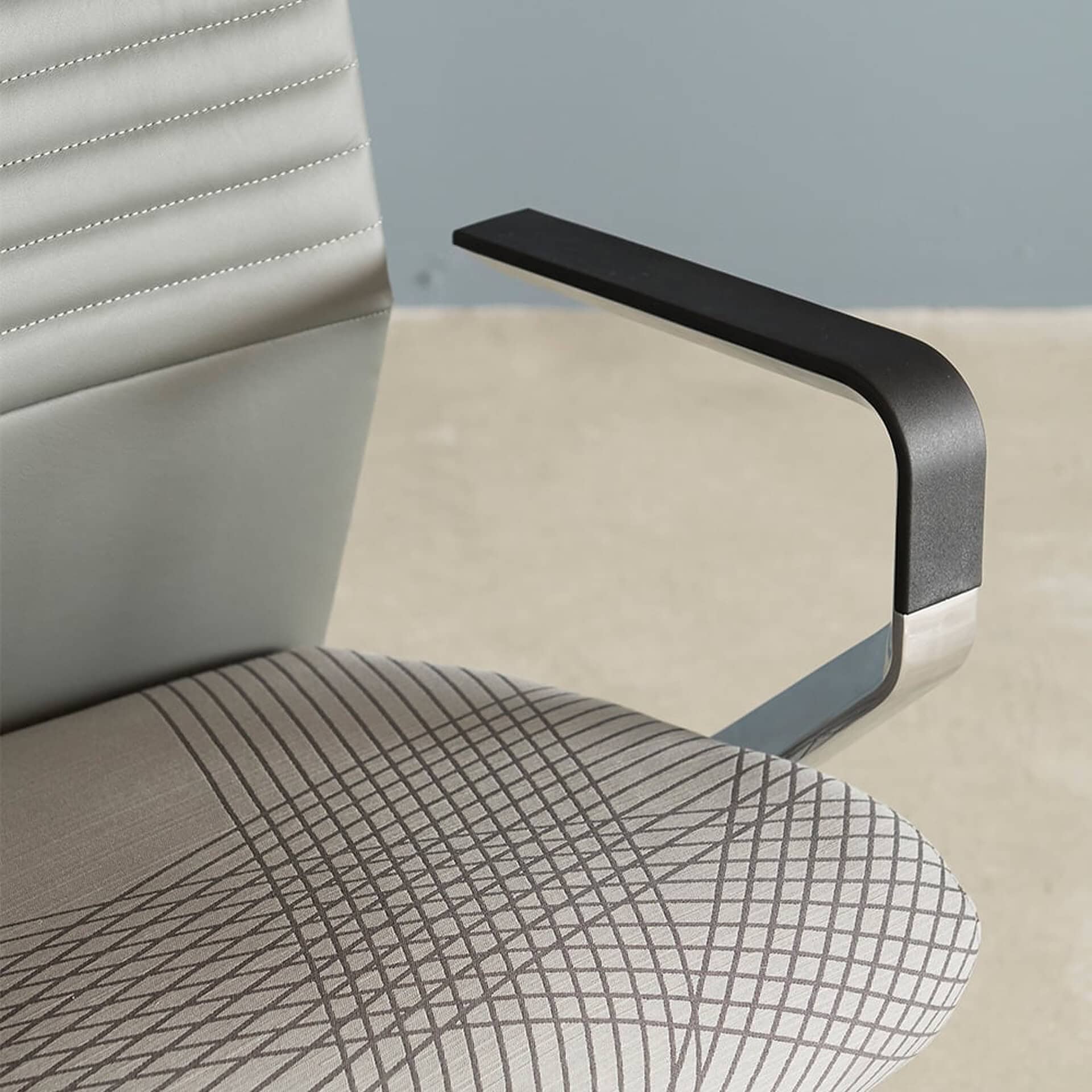 Close-up of a modern chair showing a light gray quilted back, a beige patterned fabric seat, and a black and chrome armrest.