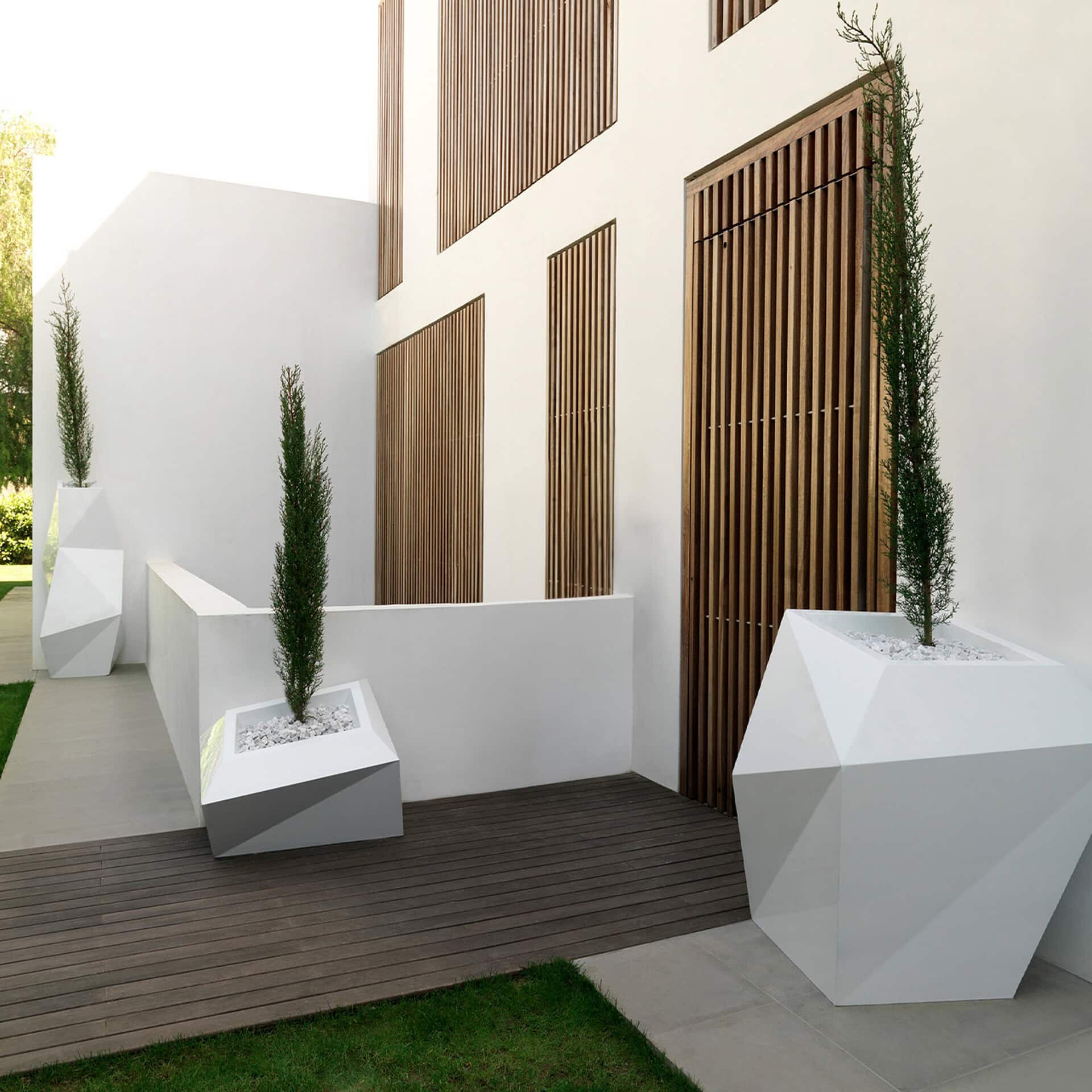 Contemporary white geometric planters with tall green plants on a wooden deck.