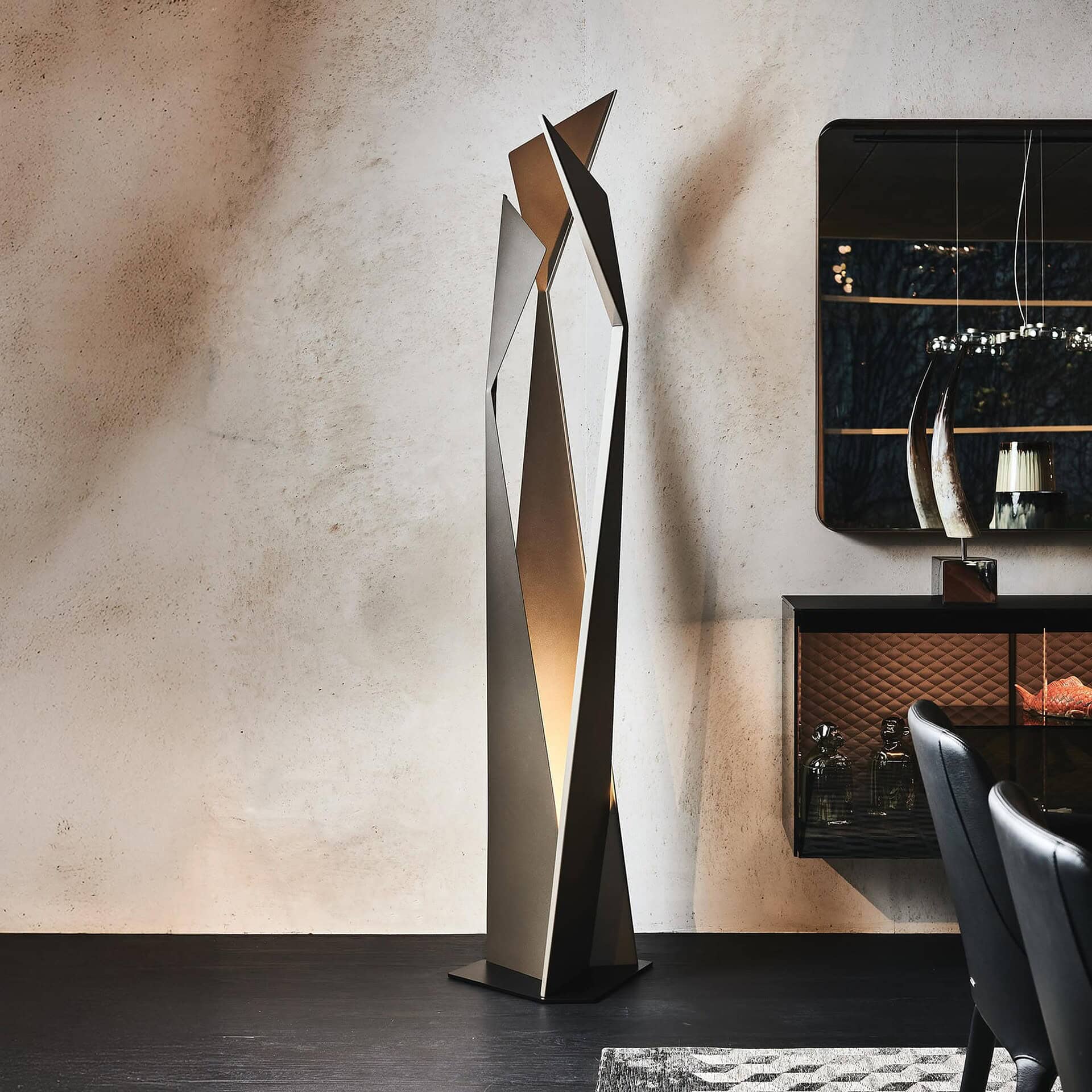 Thriller Sculptural Floor Lamp in embossed bronze steel, placed in a modern living room beside a black cabinet and neutral-toned wall.