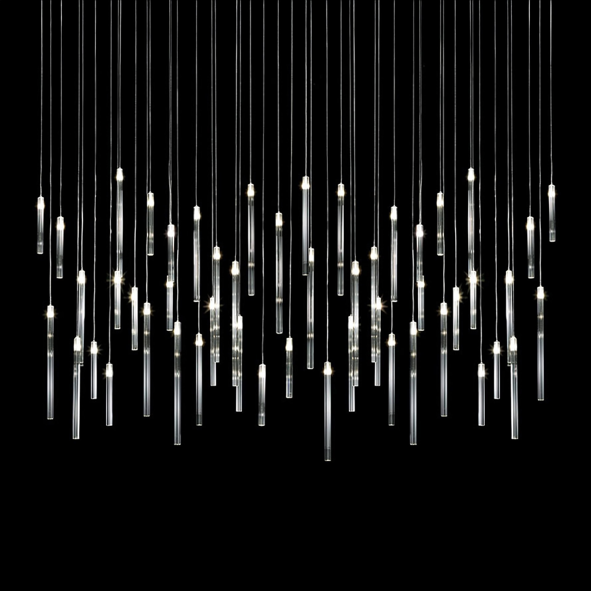 Modern chandelier with multiple vertical glass tube pendants illuminated against a black background.