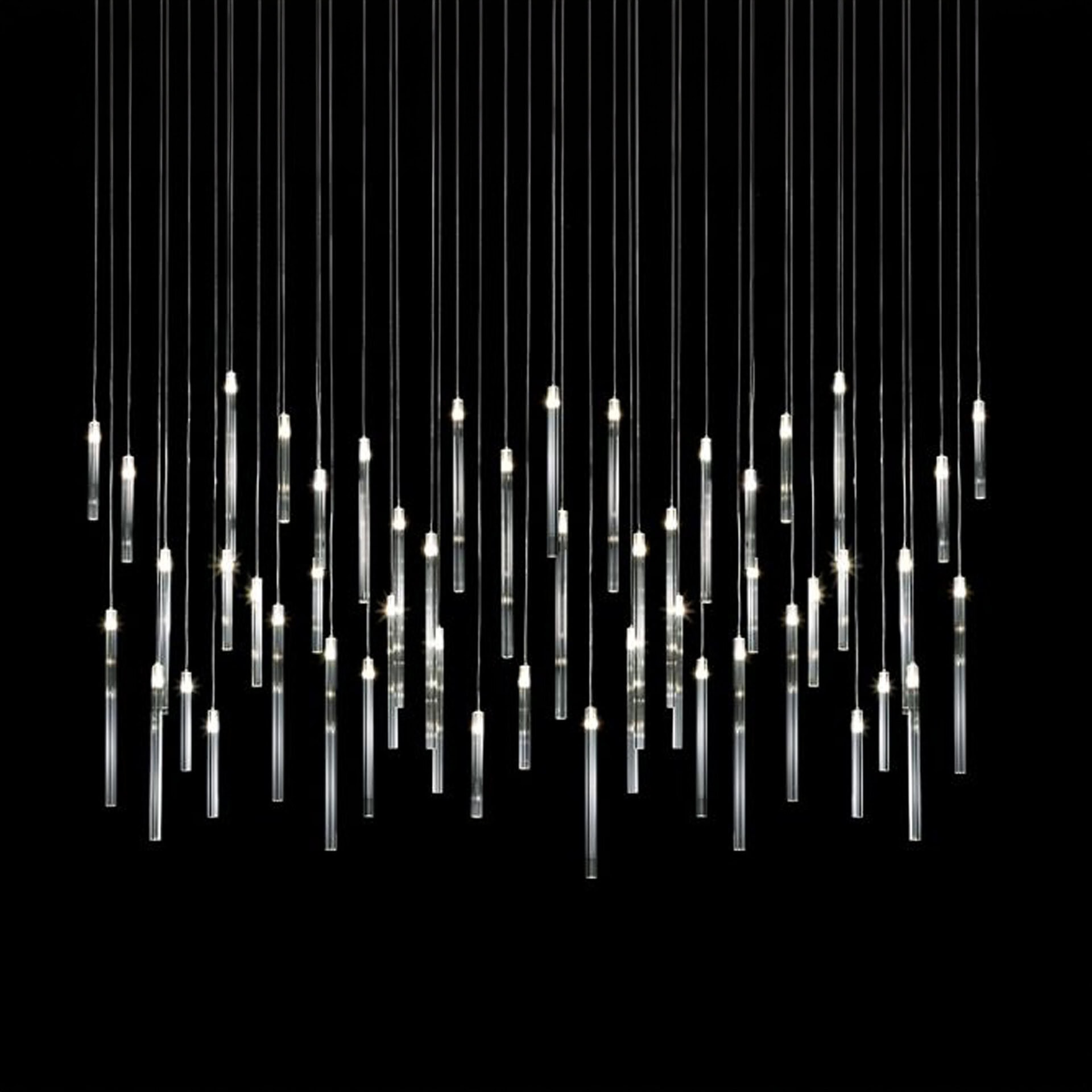 Modern chandelier with multiple vertical glass tube pendants illuminated against a black background.