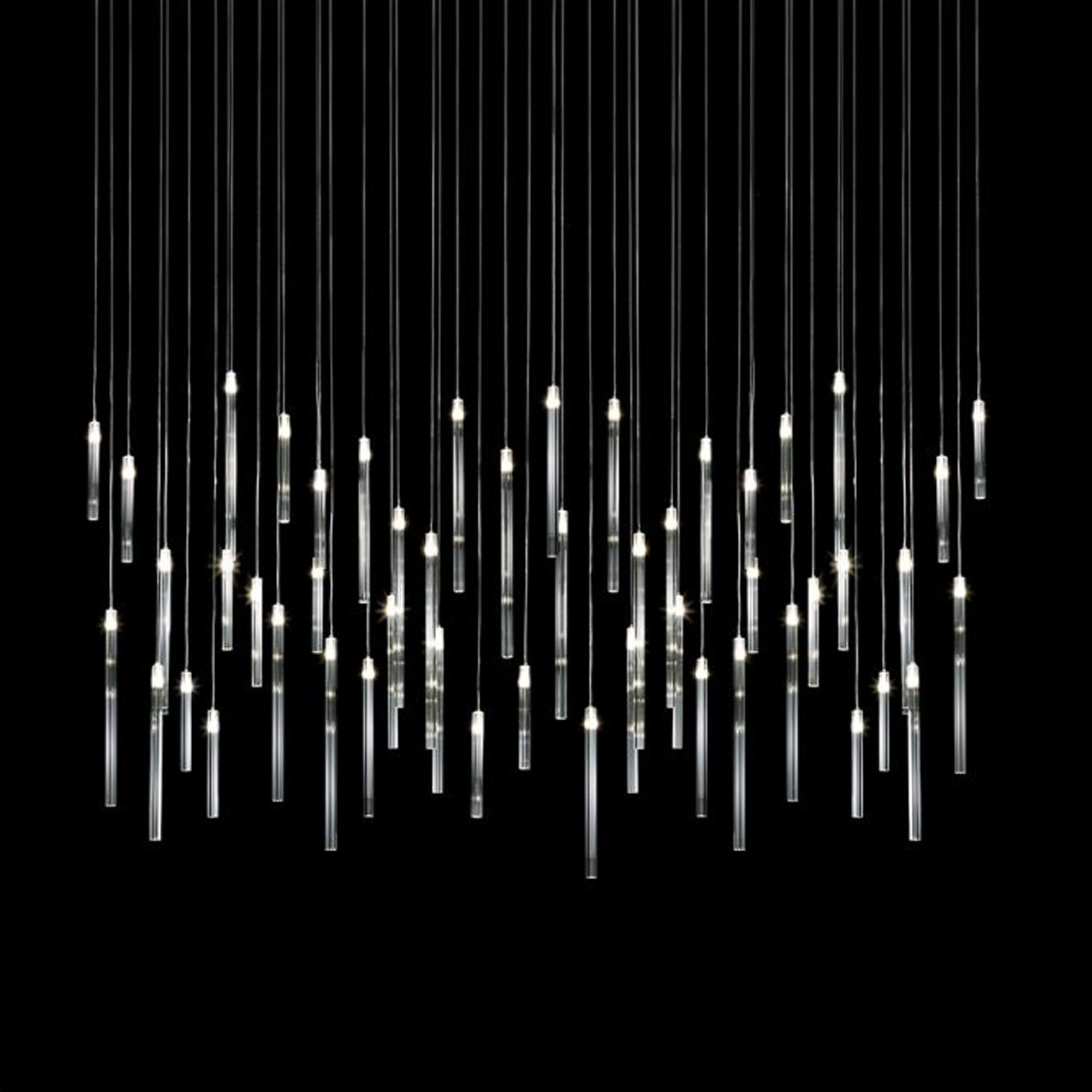 Modern chandelier with multiple vertical glass tube pendants illuminated against a black background.