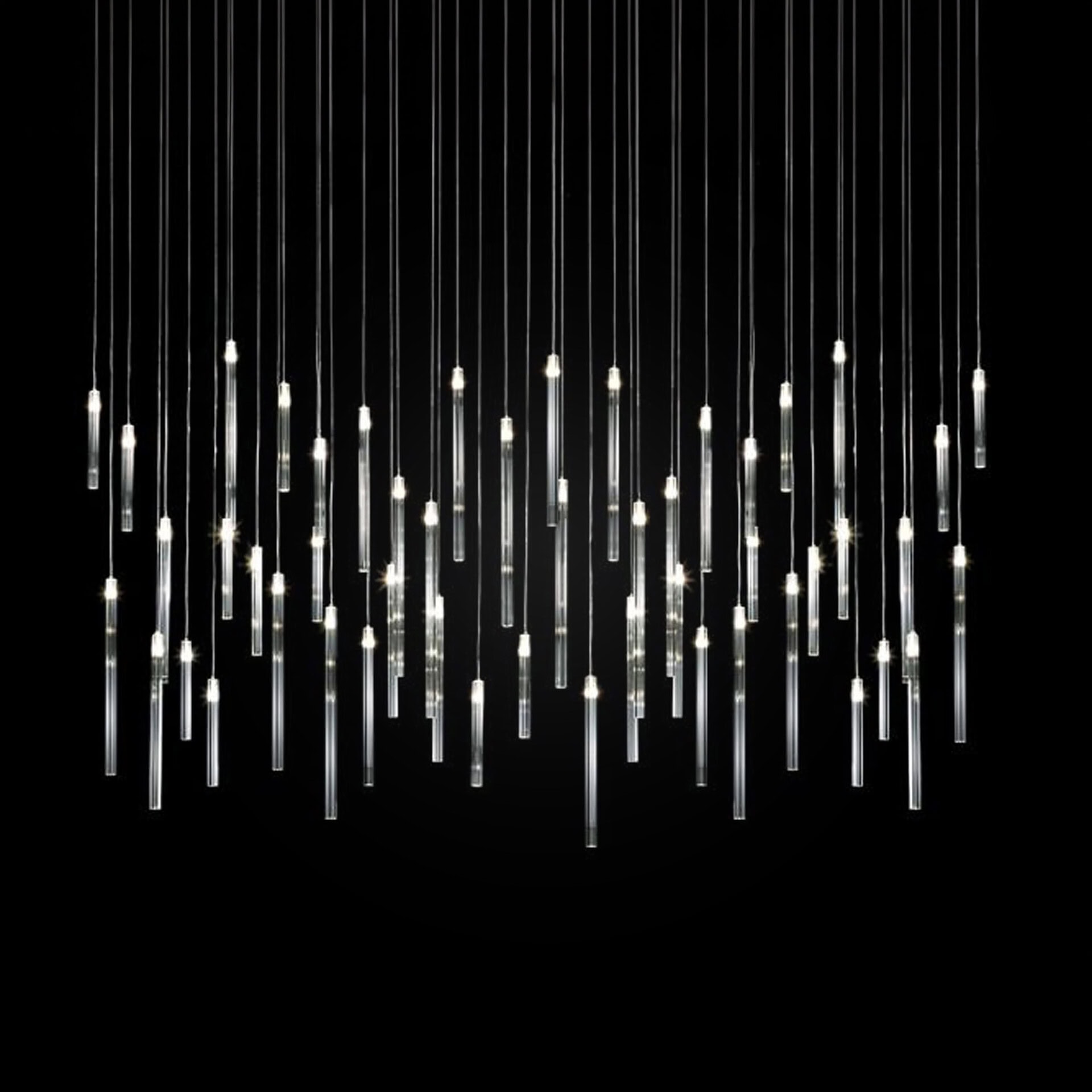 Modern chandelier with multiple vertical glass tube pendants illuminated against a black background.