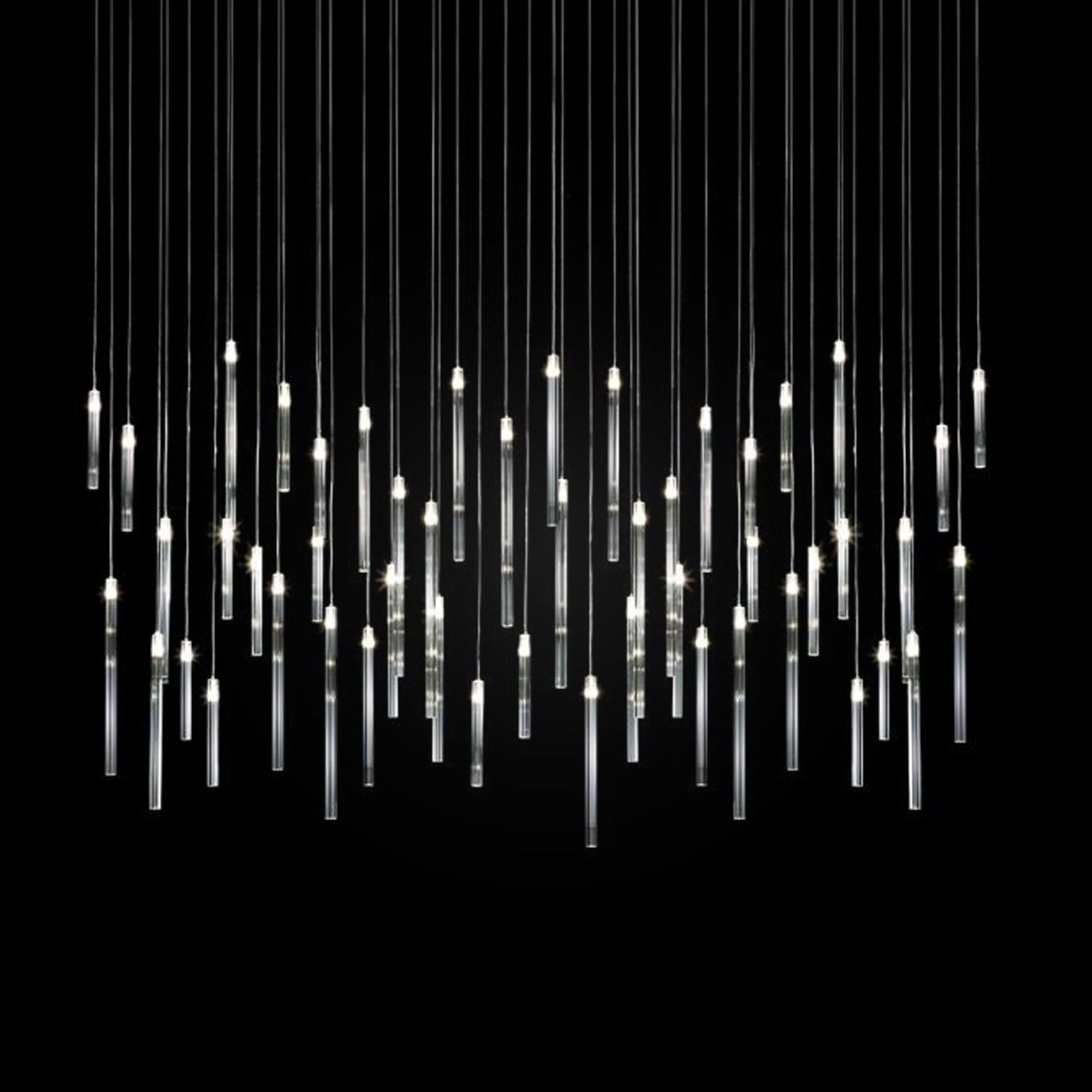 Modern chandelier with multiple vertical glass tube pendants illuminated against a black background.