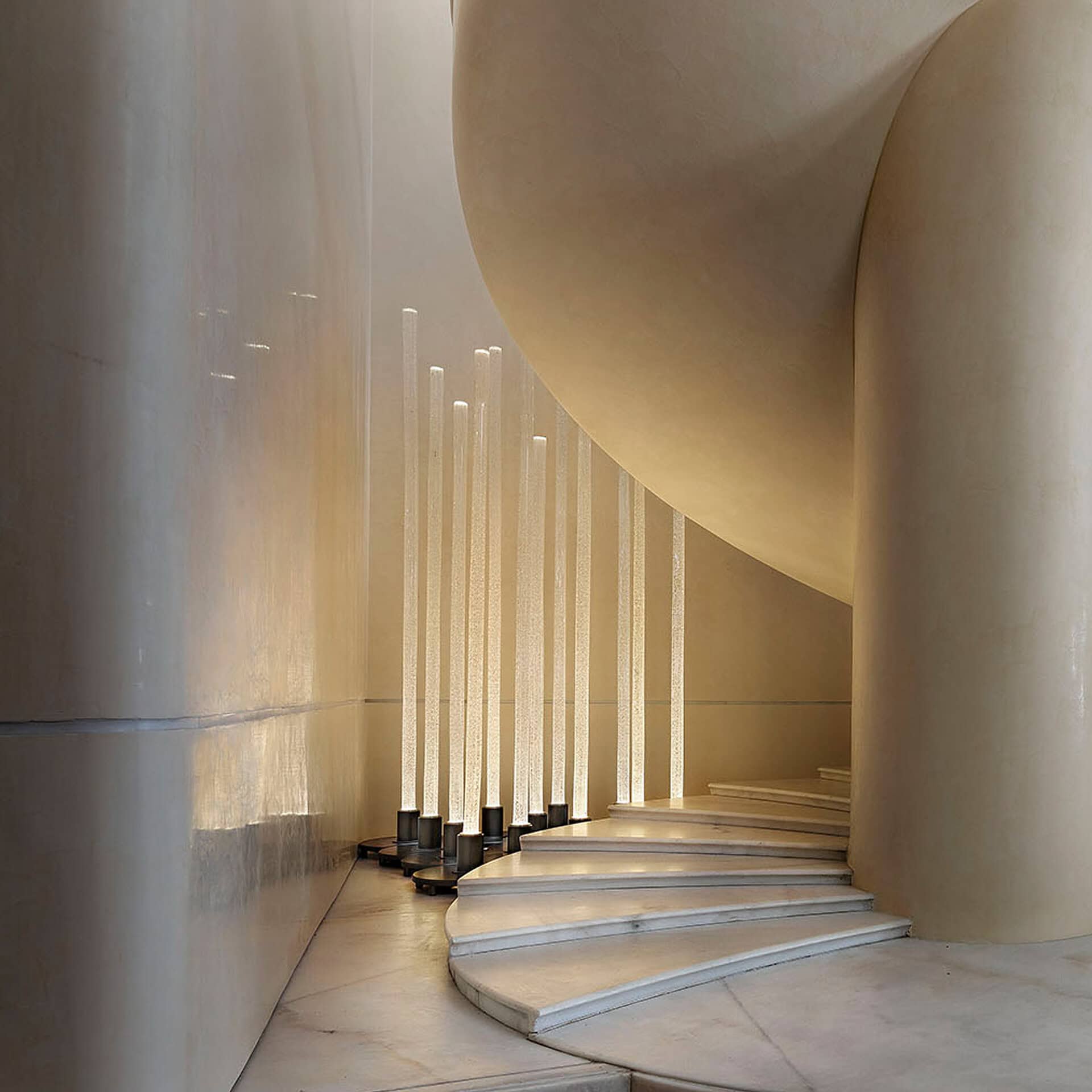 Modern interior design with curved staircase and vertical light fixtures.