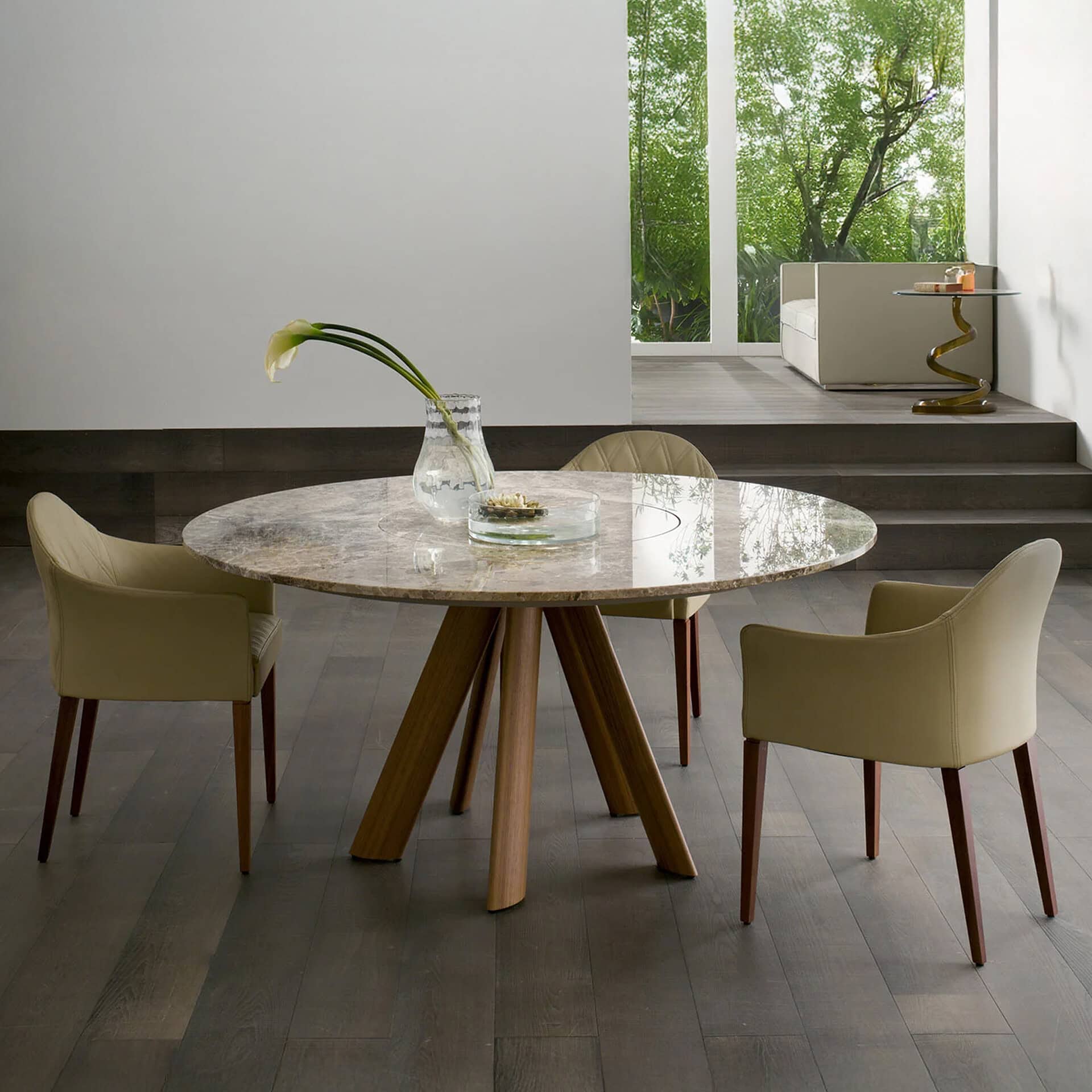 Elegant dining room featuring a marble table and beige chairs with large windows and greenery outsid.