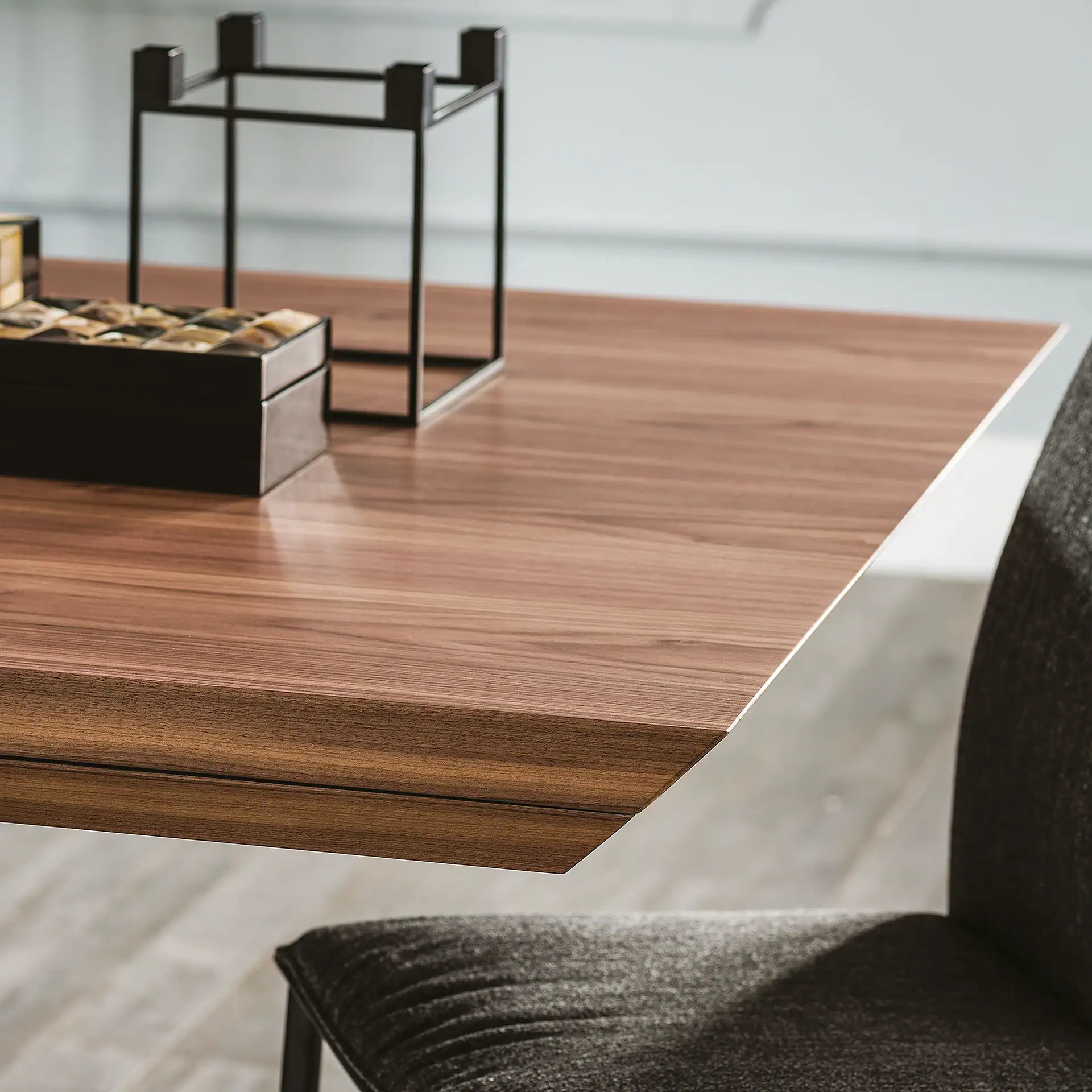 A modern brown wooden table with a black decorative box and metal object, next to a dark grey chair.