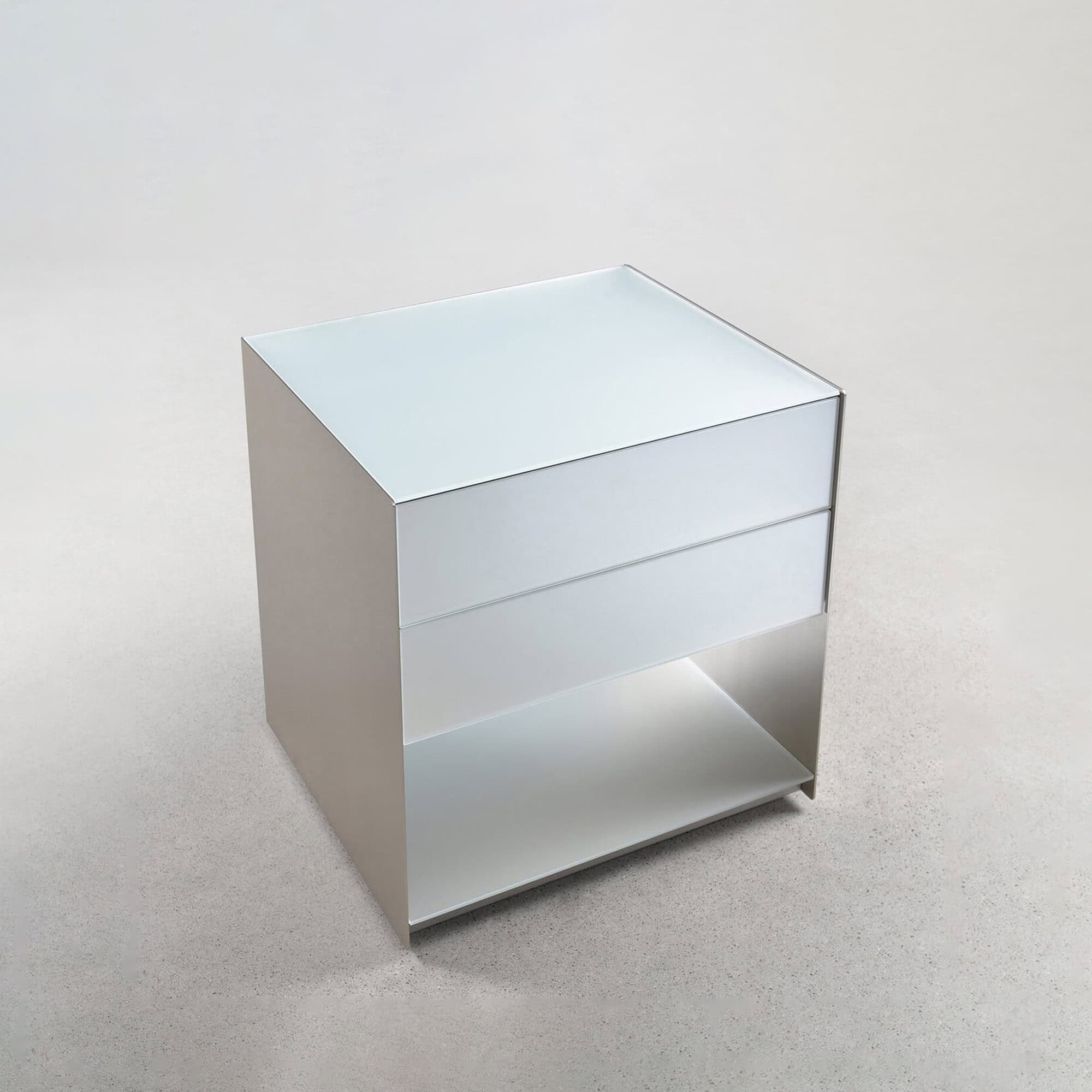 A modern, minimalist light gray bedside table with a reflective top, one drawer, and an open shelf, against a light gray background.
