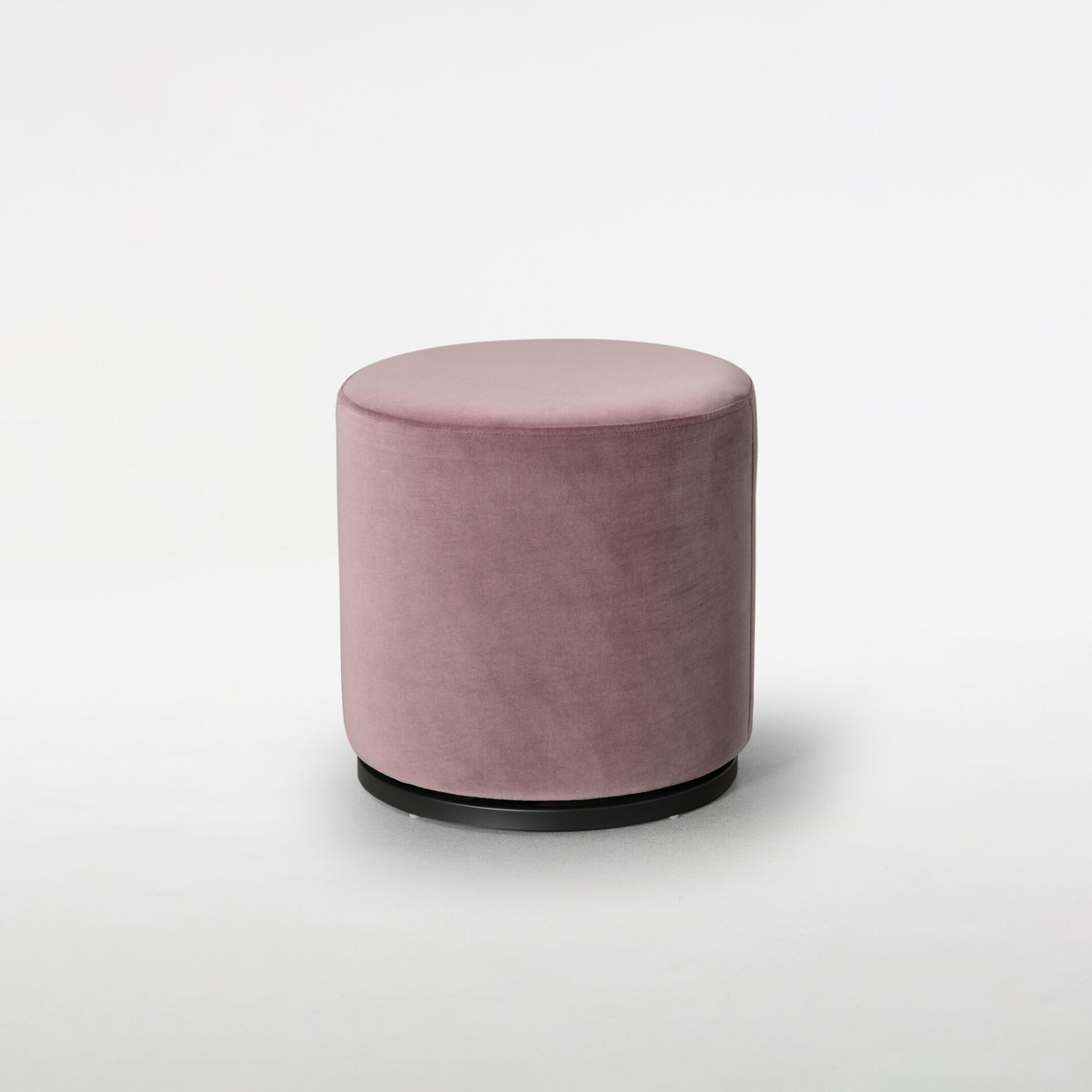 A cylindrical dusty pink velvet ottoman with a black base, isolated on a white background.