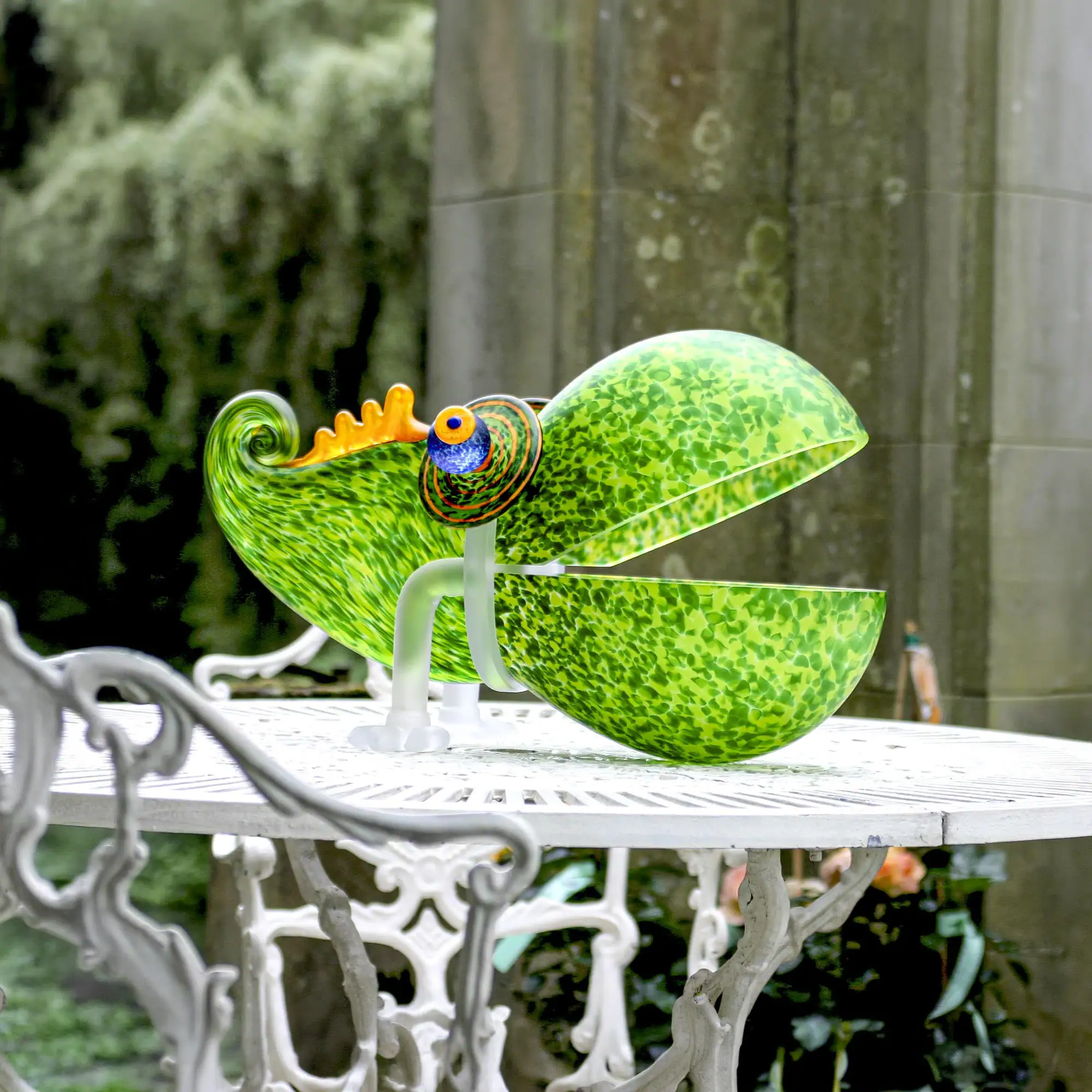 Chameleon Big Glass Bowl with an open mouth and a curled tail, featuring a blue and orange eye, sits on a white metal outdoor table.