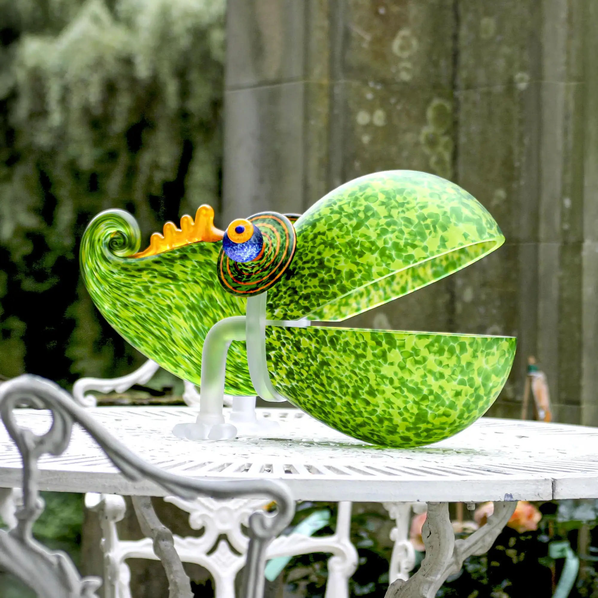 Chameleon Big Glass Bowl with an open mouth and a curled tail, featuring a blue and orange eye, sits on a white metal outdoor table.