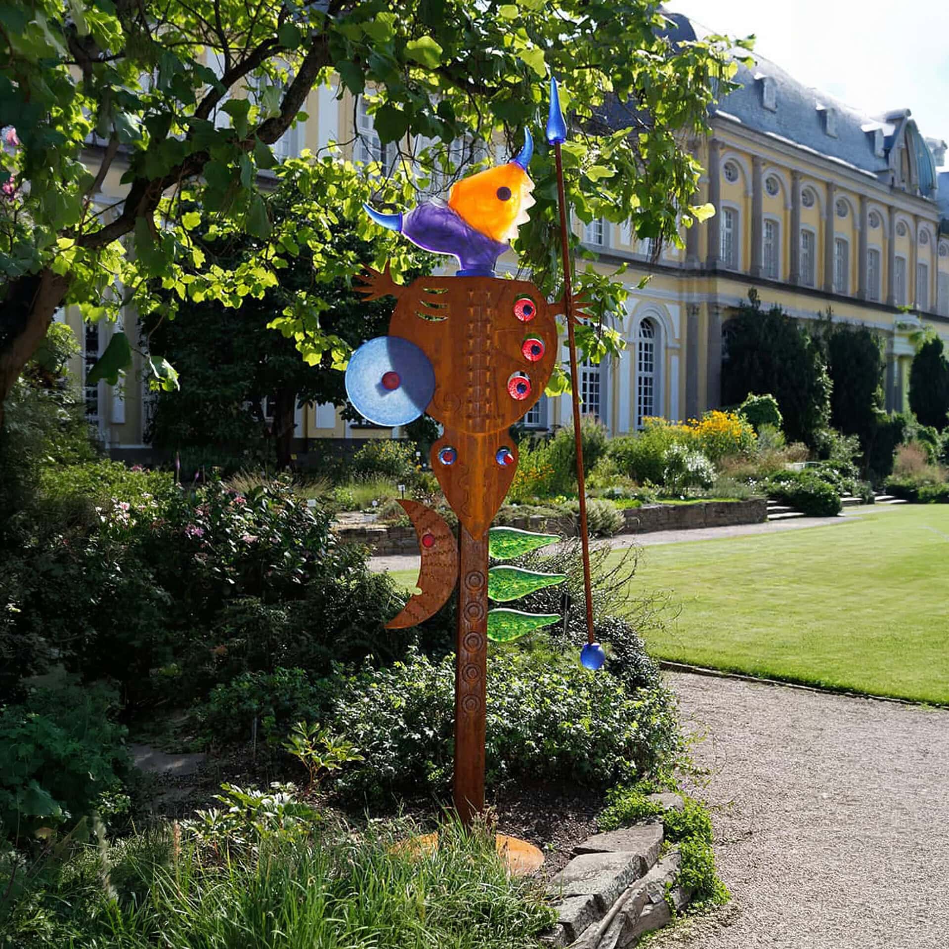 Colorful fish-shaped wind chime sculpture in a lush garden setting.