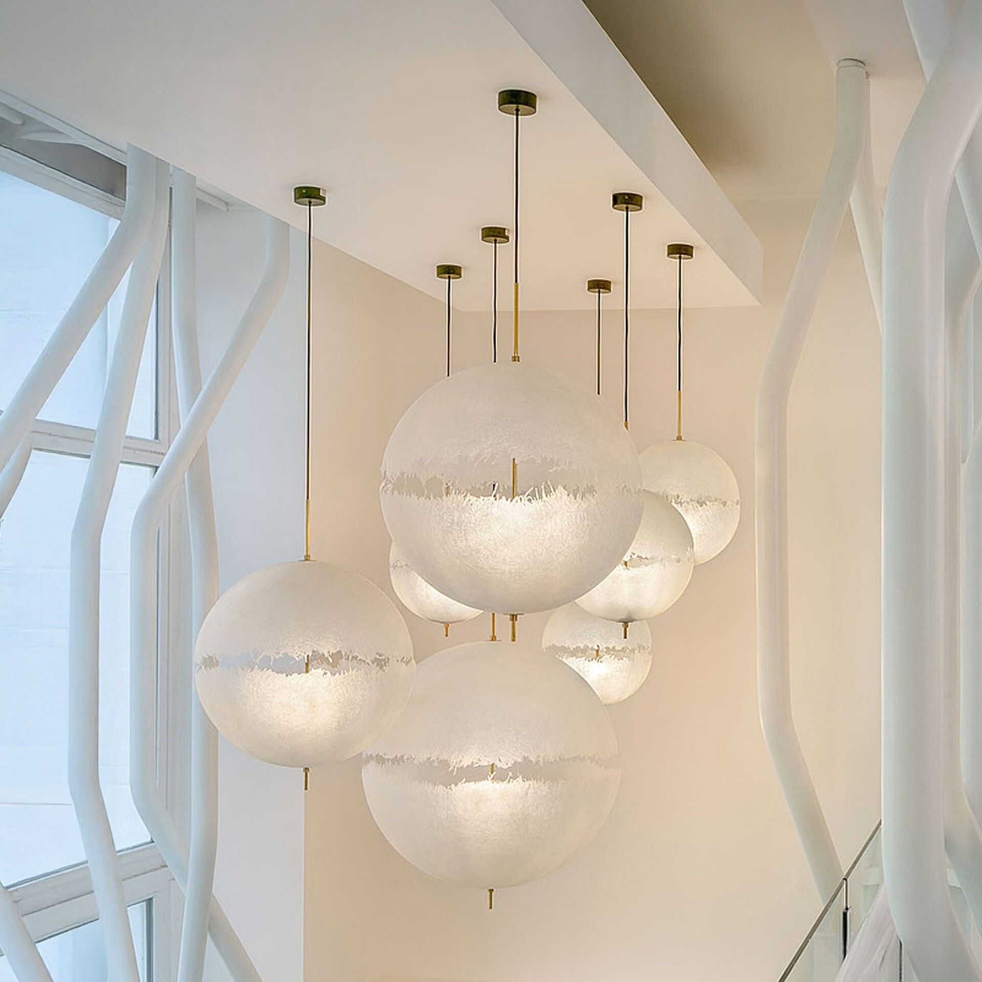 Multiple PostKrisi pendant lights hanging in a modern white interior, showcasing varied heights and soft diffused glow.