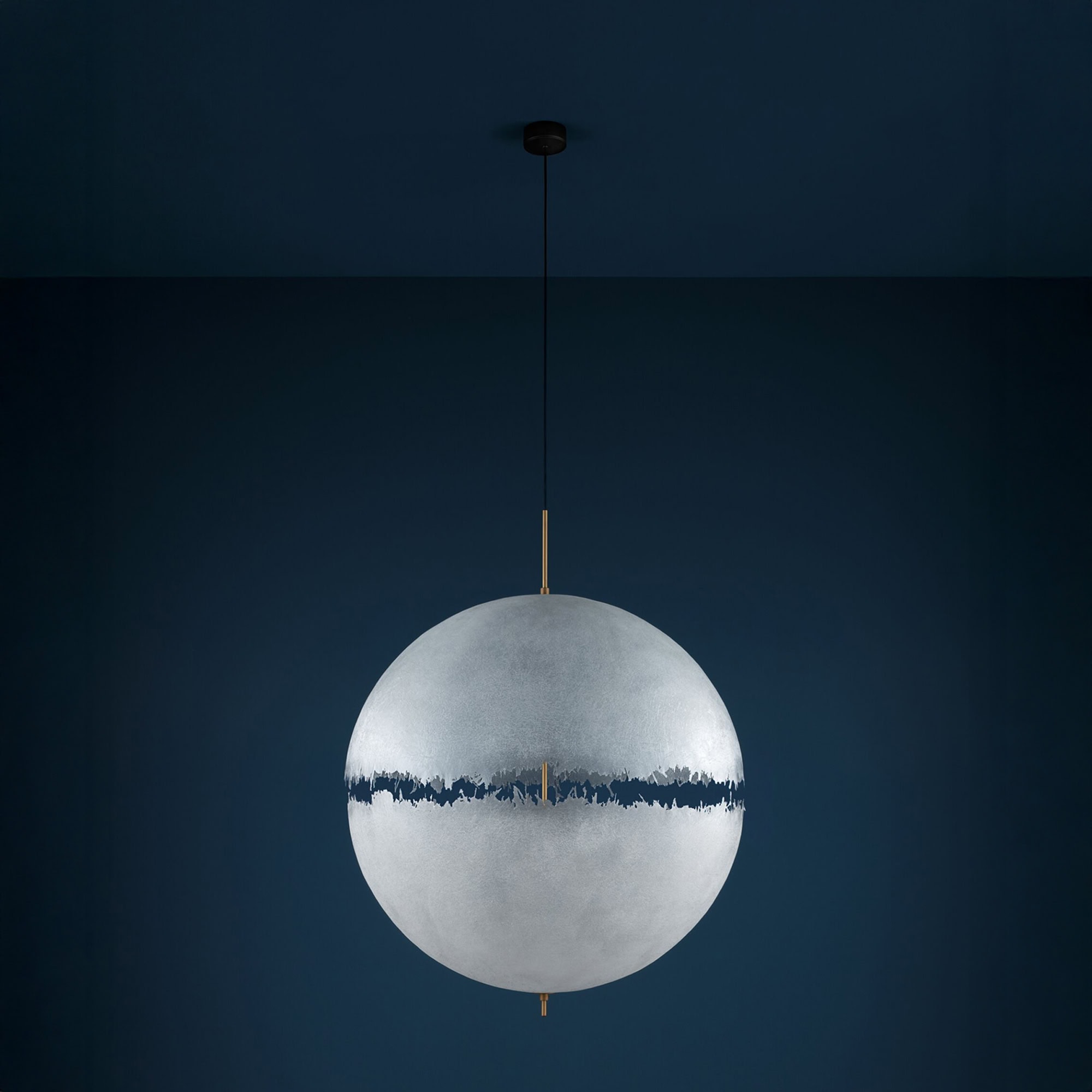 Single PostKrisi pendant light with brass rod against a dark blue background, showing close-up of handcrafted texture.