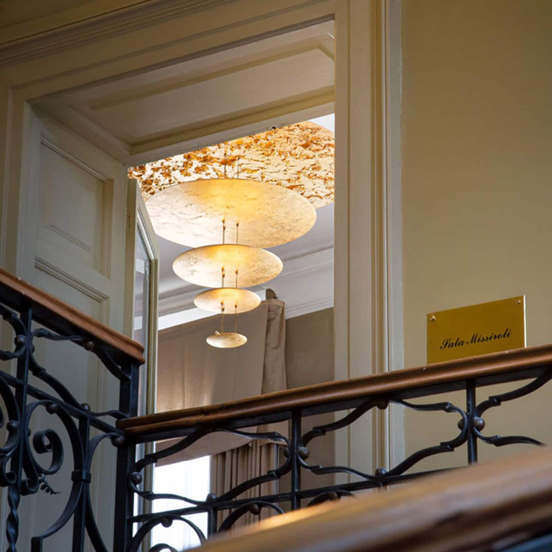 Macchina della Luce Pendant Light hanging above a staircase with golden reflections.