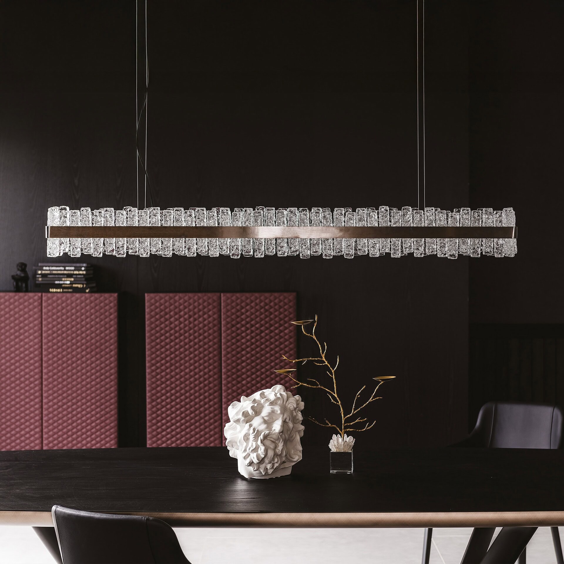 Phoenix LED Handmade Glass Chandelier above dining table against dark wall with red panels.