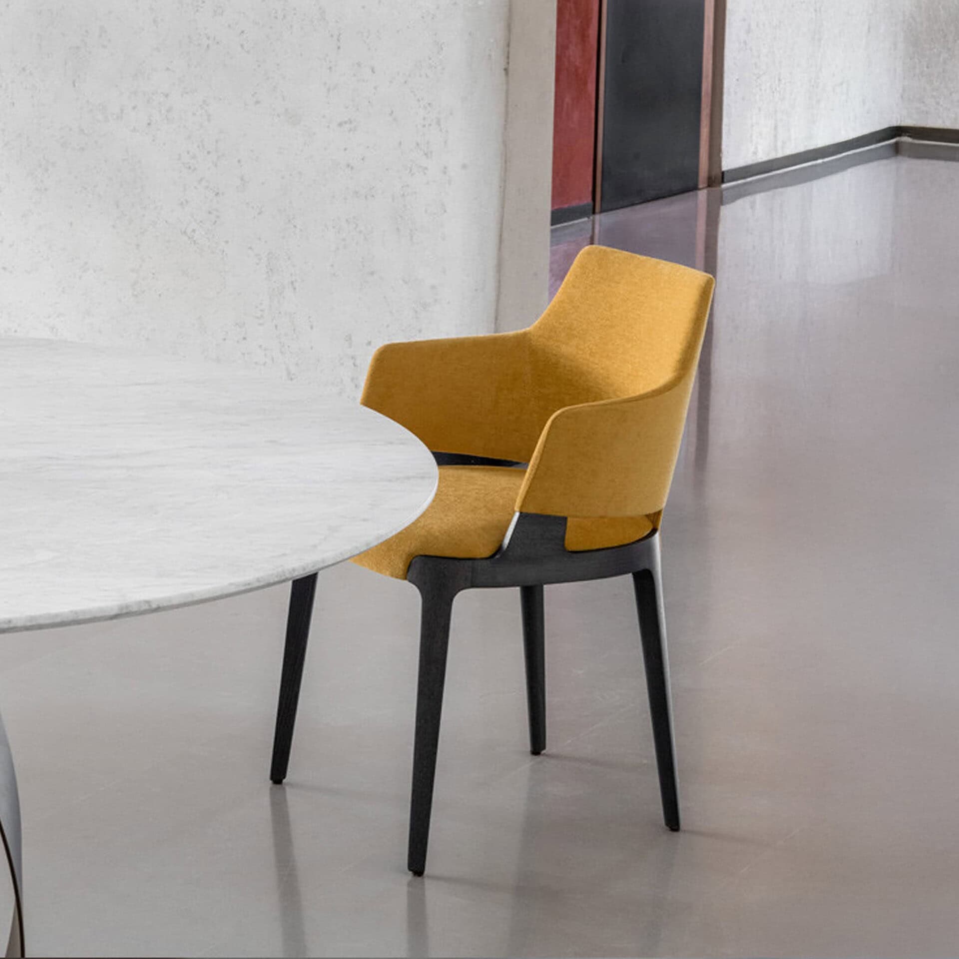 Yellow upholstered Velis dining chair with wooden legs beside a round marble table.