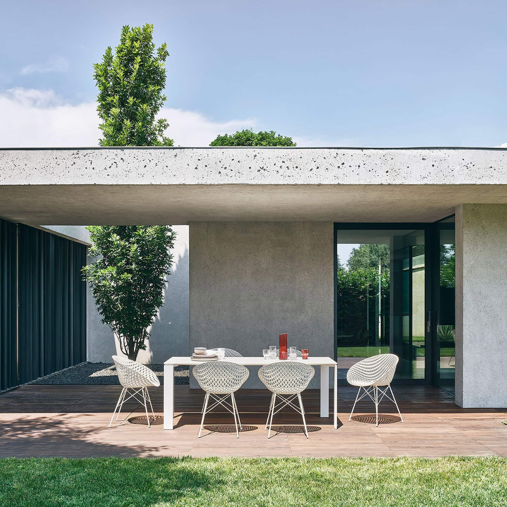 White Smatrik Chairs arranged around an outdoor dining table in a contemporary garden patio.