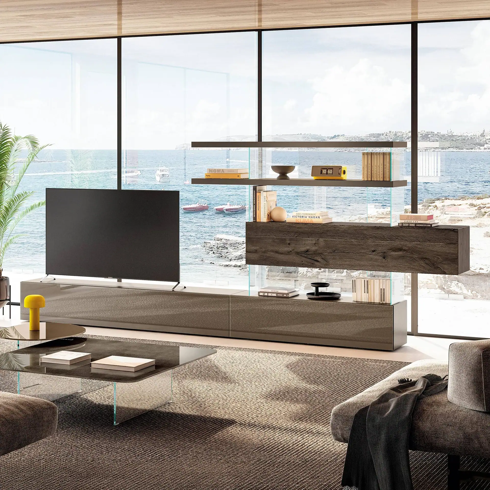 A modern living room with a large TV, sleek shelving unit, and sofa, all facing expansive windows that overlook a blue sea with boats and a distant coastline.