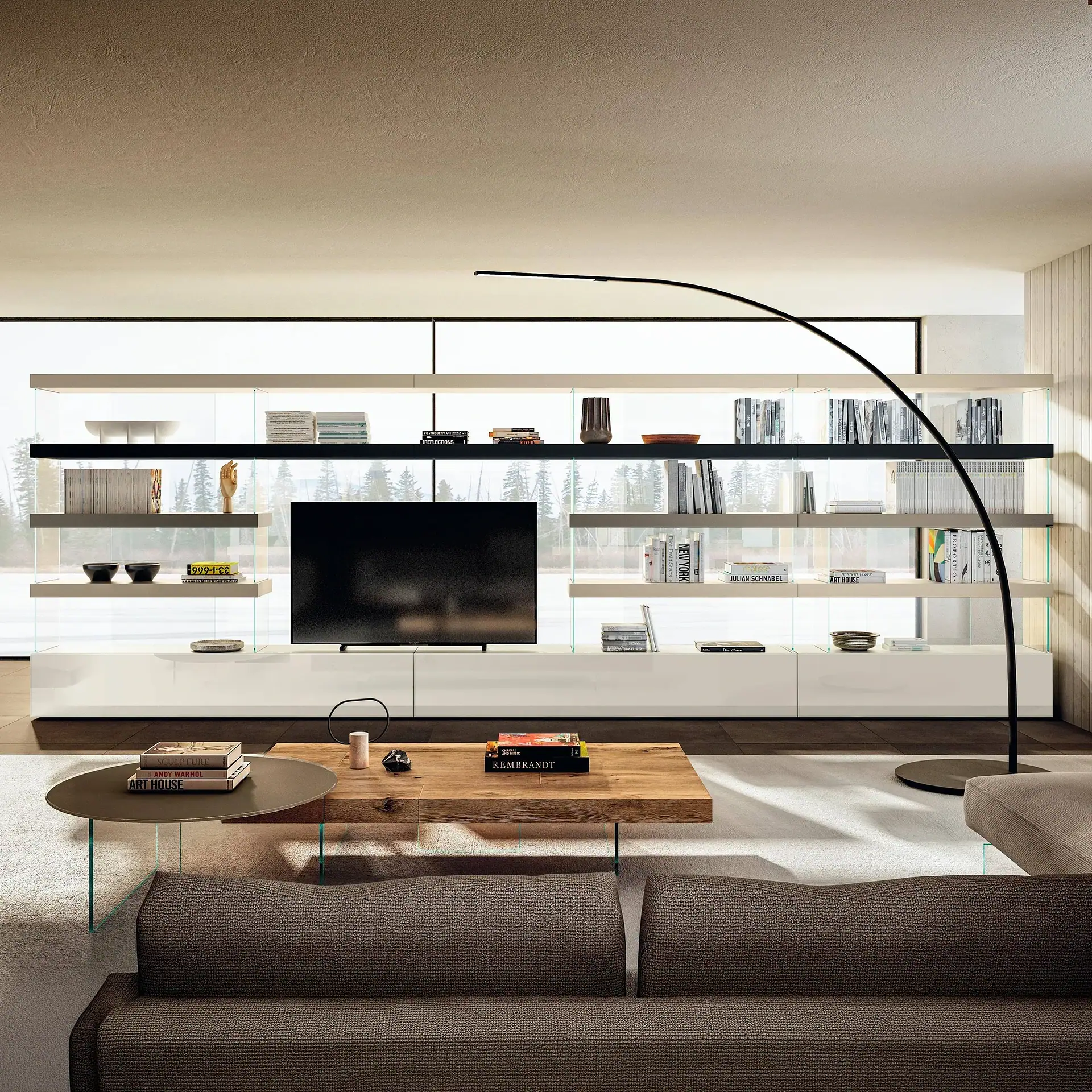 A modern living room with a large media console, television, and shelves filled with books and decor, facing a dark brown sofa and coffee tables. A large window behind the console offers a view of a snowy forest.