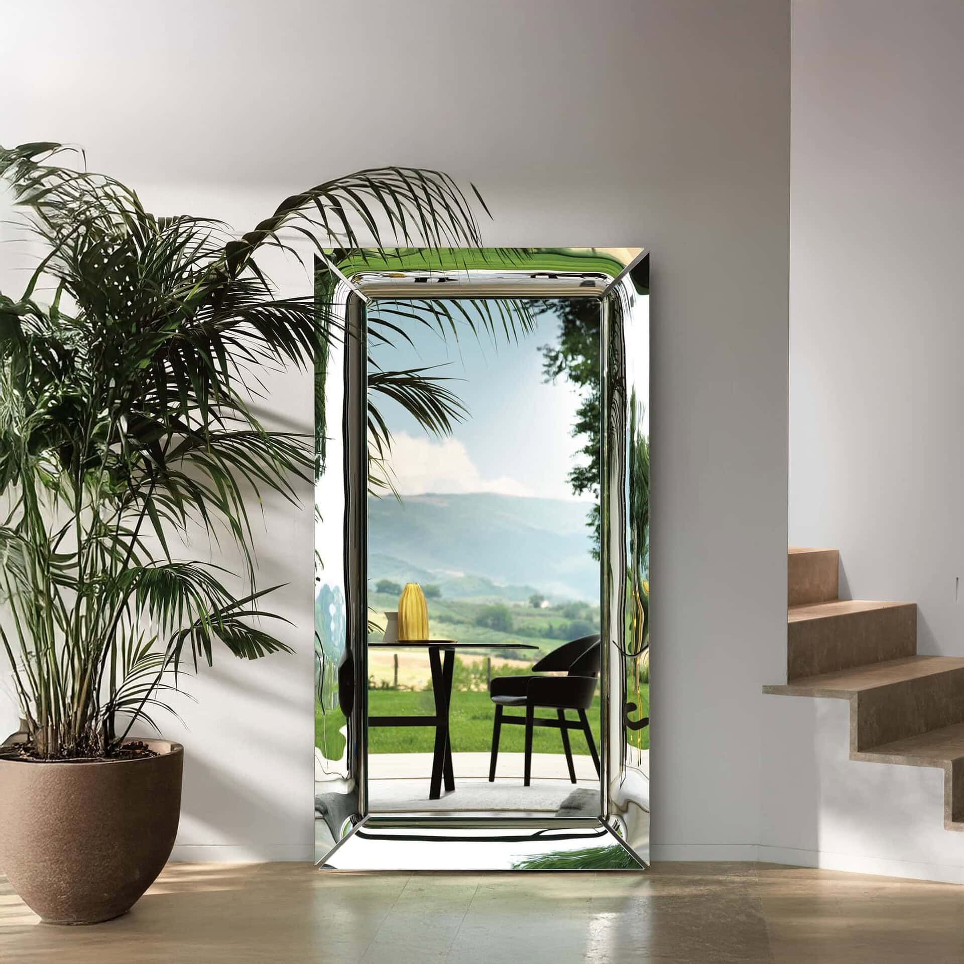 Tall free-standing Caadre Mirror with bronze finish in a bright interior with greenery.