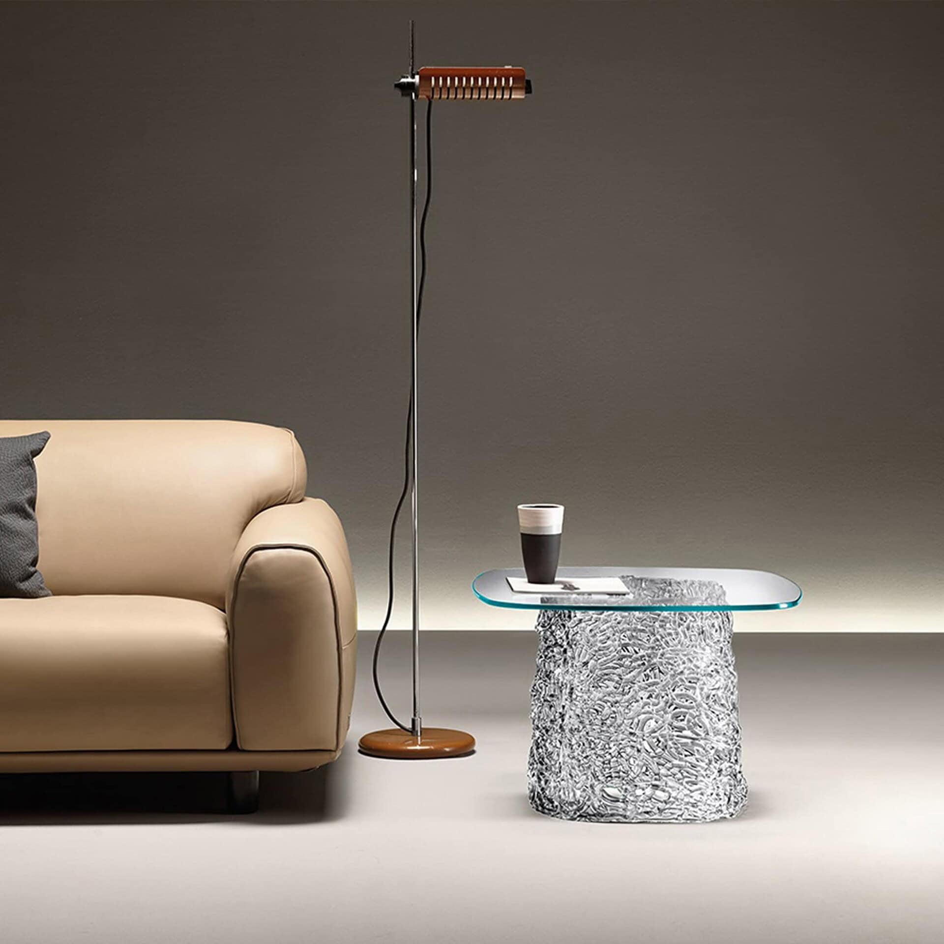 Macramè Coffee Table in fumè grey glass finish placed beside a sofa in a modern setting