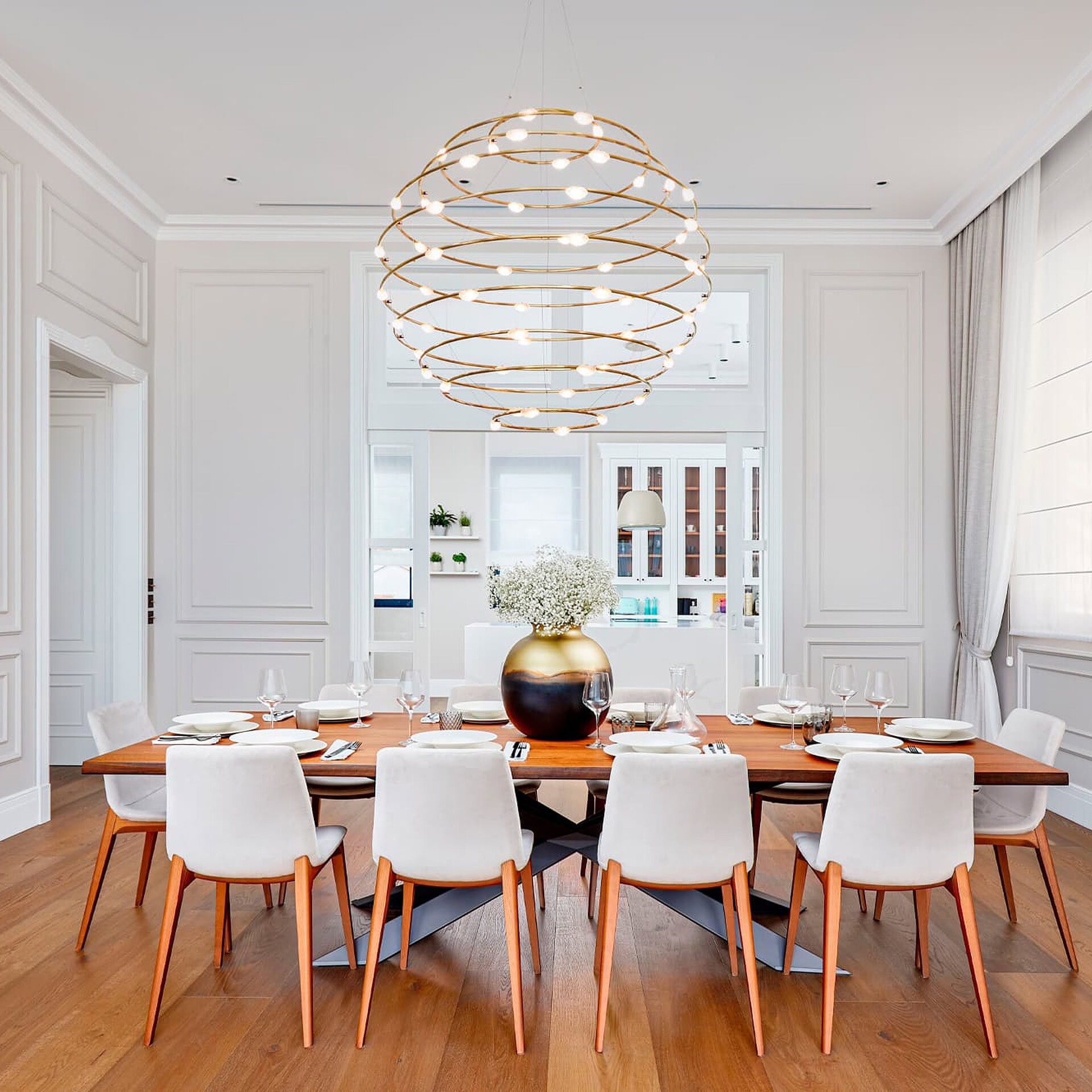 Elegant white dining room with modern chandelier and wooden table.