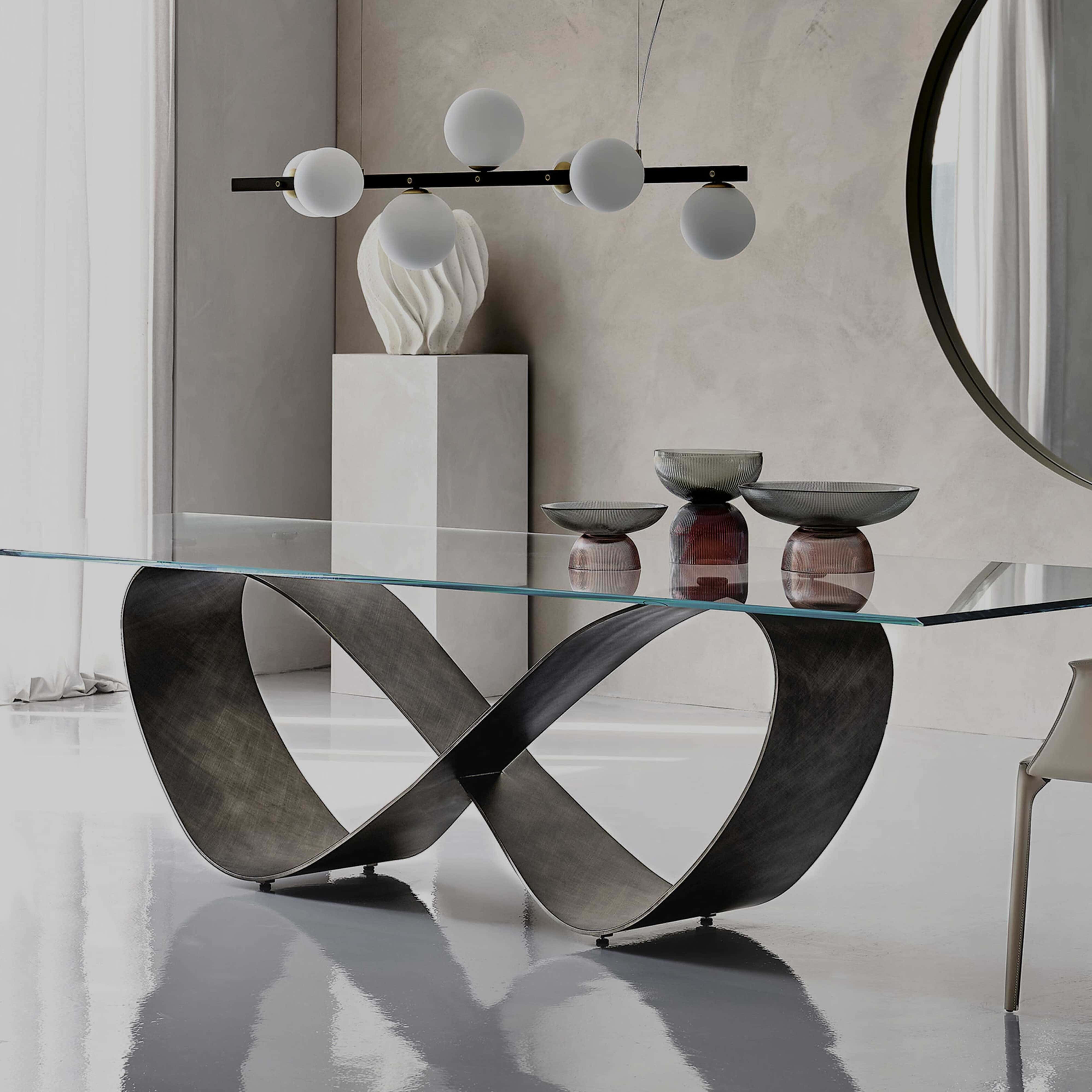 Contemporary glass dining table with sculptural metal base, modern lighting, and stylish decor.