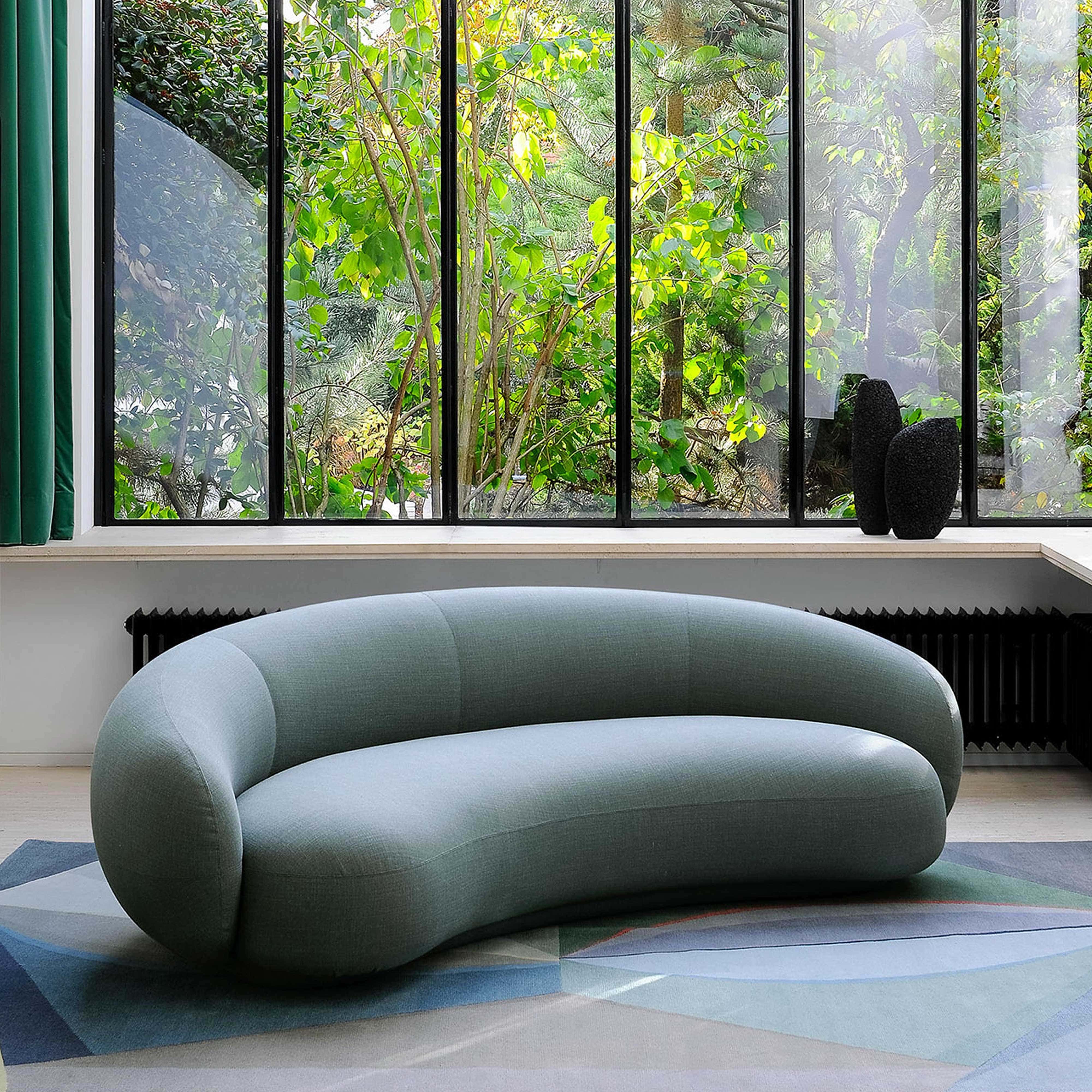 Luxurious modern green sofa in bright living room with large window and nature view.