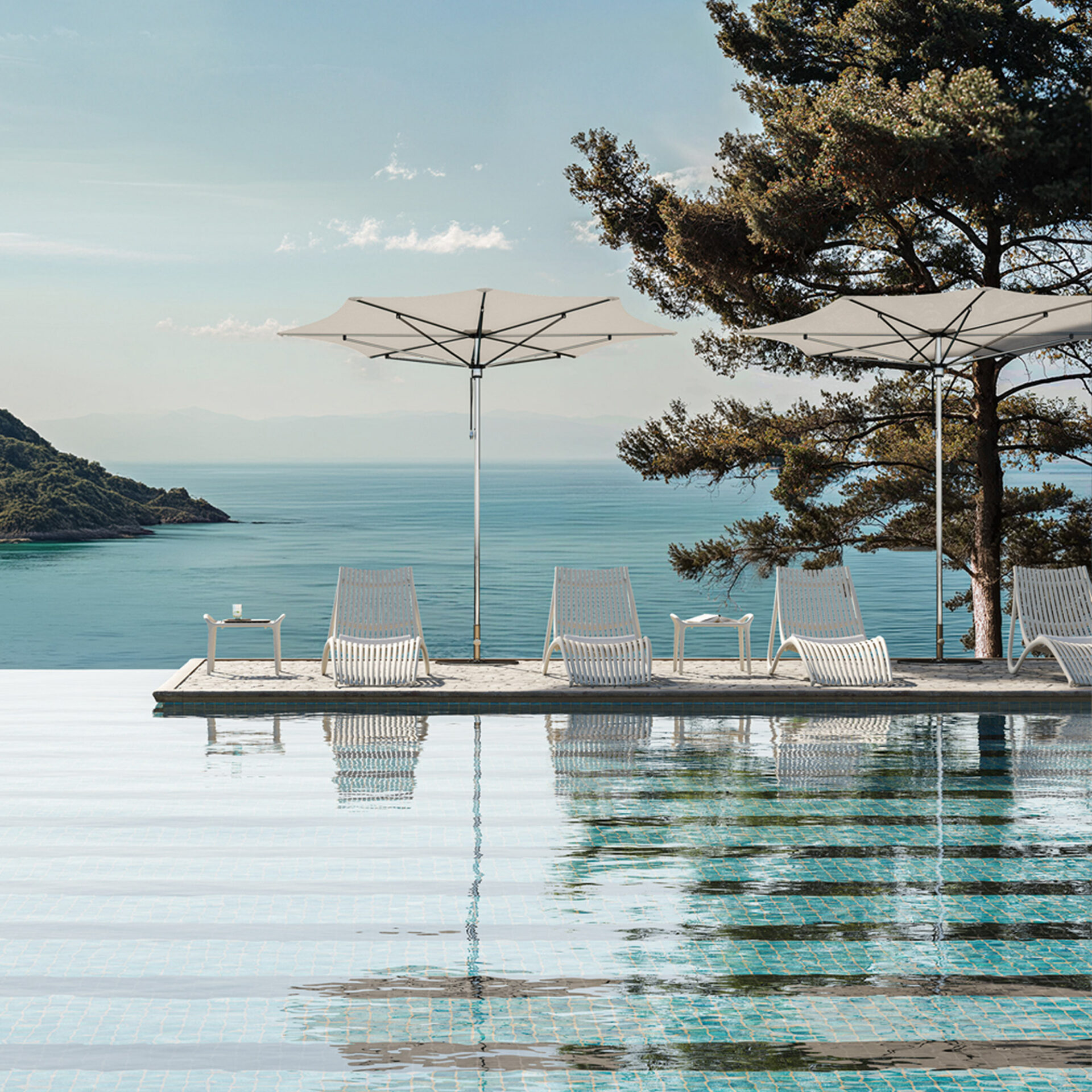 An infinity pool with modern white lounge chairs and umbrellas overlooking a vast, calm turquoise ocean and distant green islands under a clear sky.