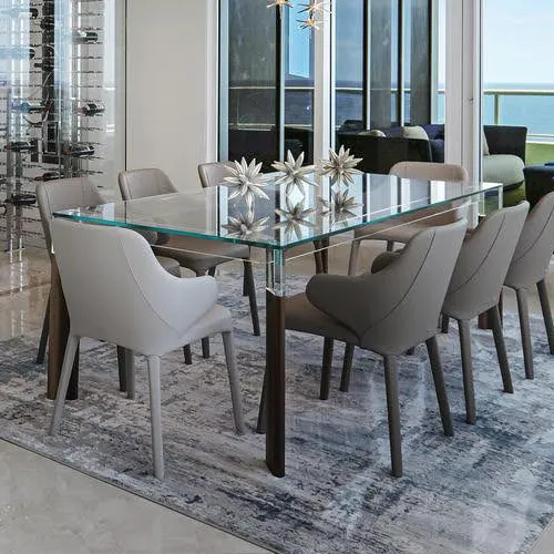 A modern dining room with a square glass table, eight gray upholstered chairs, and a large window overlooking the ocean.
