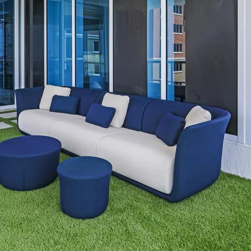 A modern outdoor sofa with blue frame and white cushions, accompanied by two blue ottomans, on artificial green turf. Large glass doors are in the background.