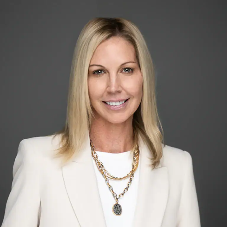 Jamie Cohen headshot smiling in white blazer against gray background.